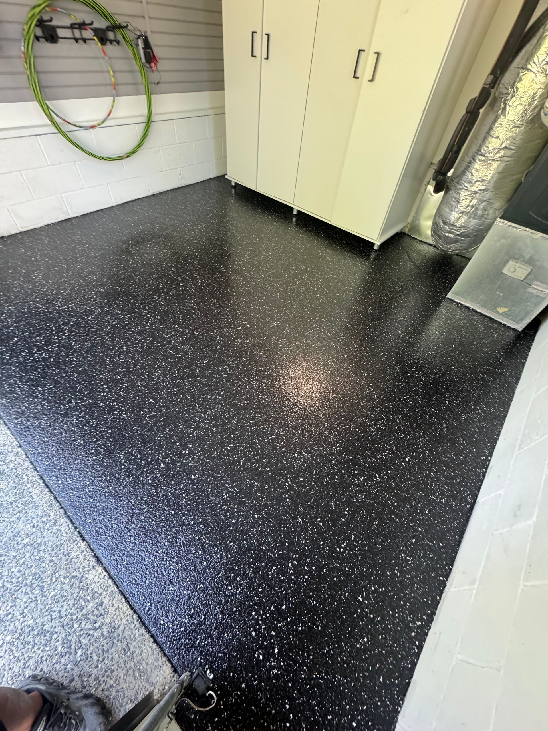 Black speckled garage floor with cabinets, hose reel, and exposed ductwork on the wall