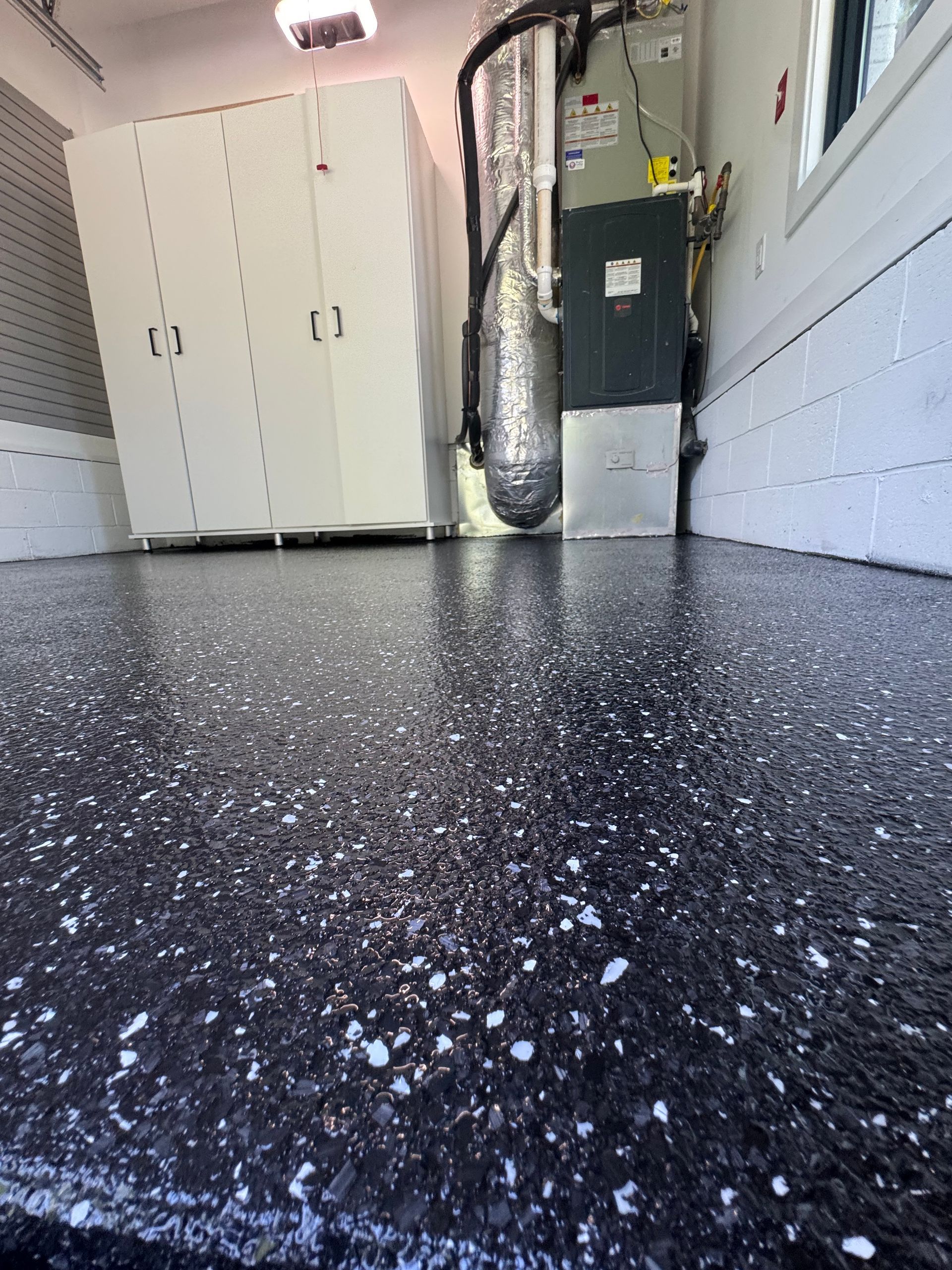 Black speckled garage floor with white cabinets, a water heater, and wall-mounted tools in a utility space
