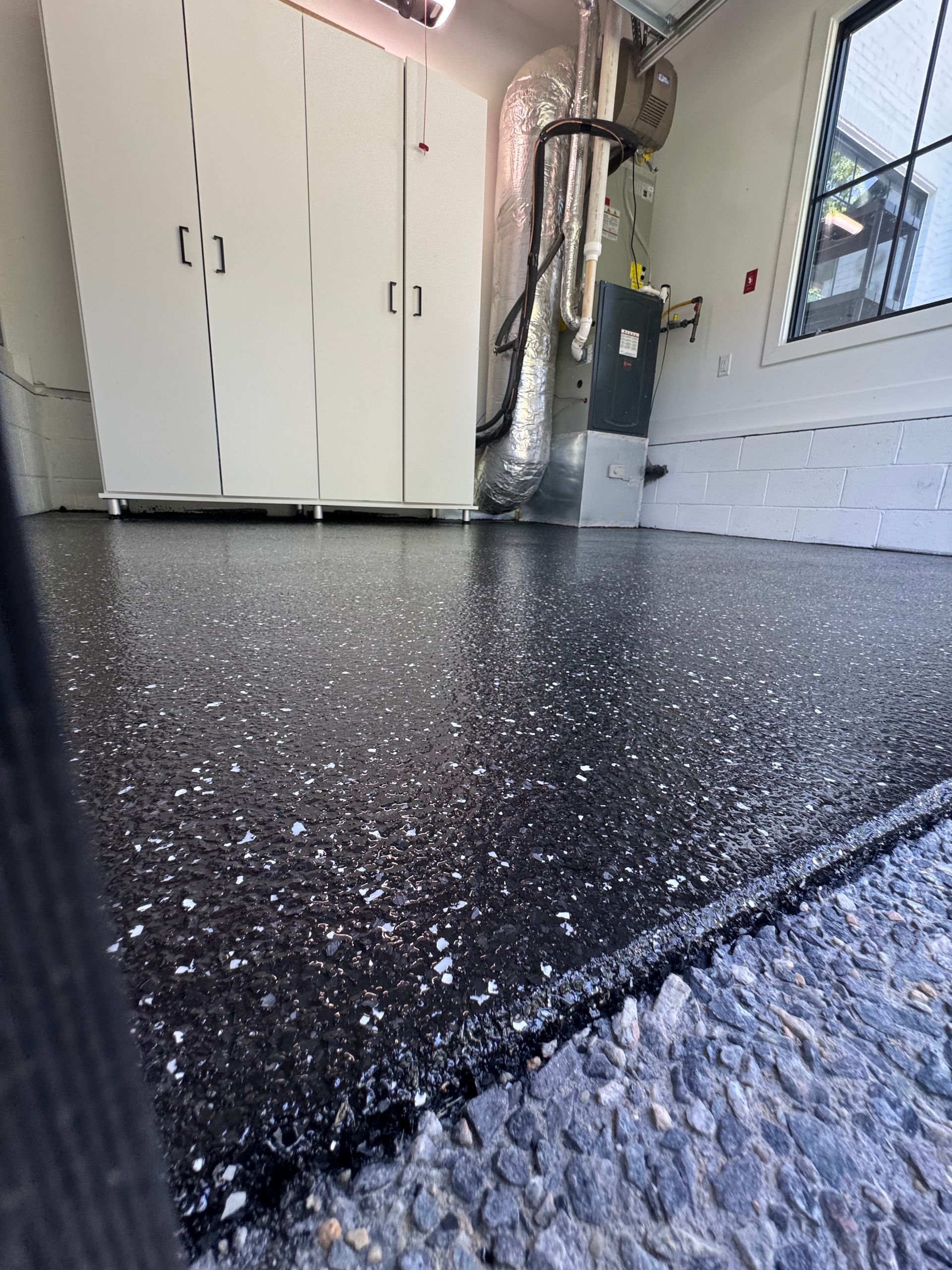 Low-angle view of a black speckled epoxy garage floor with white cabinets and a wall-mounted utility box.