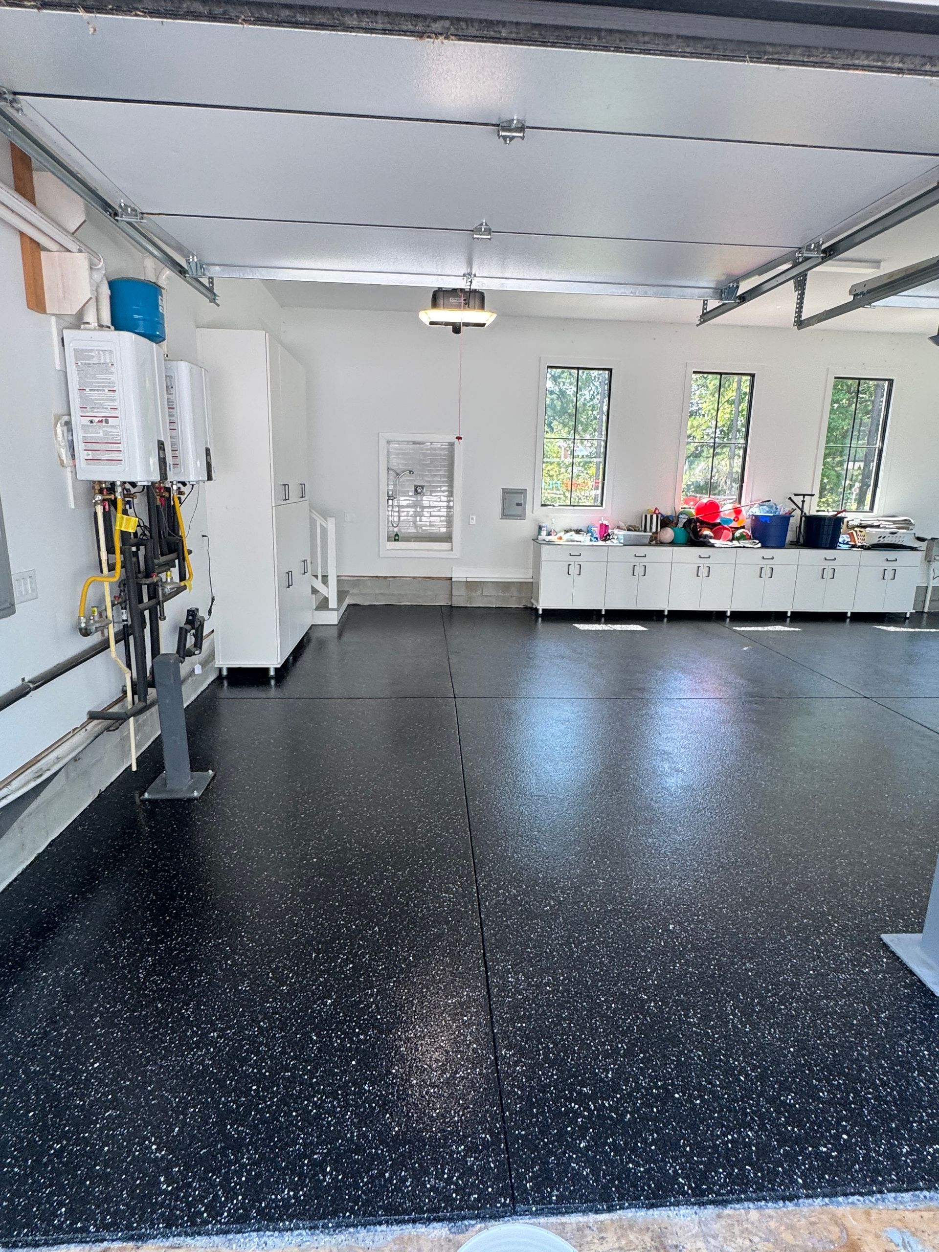 Bright garage or workshop with black speckled floor, white walls, windows, and storage cabinets along the back wall