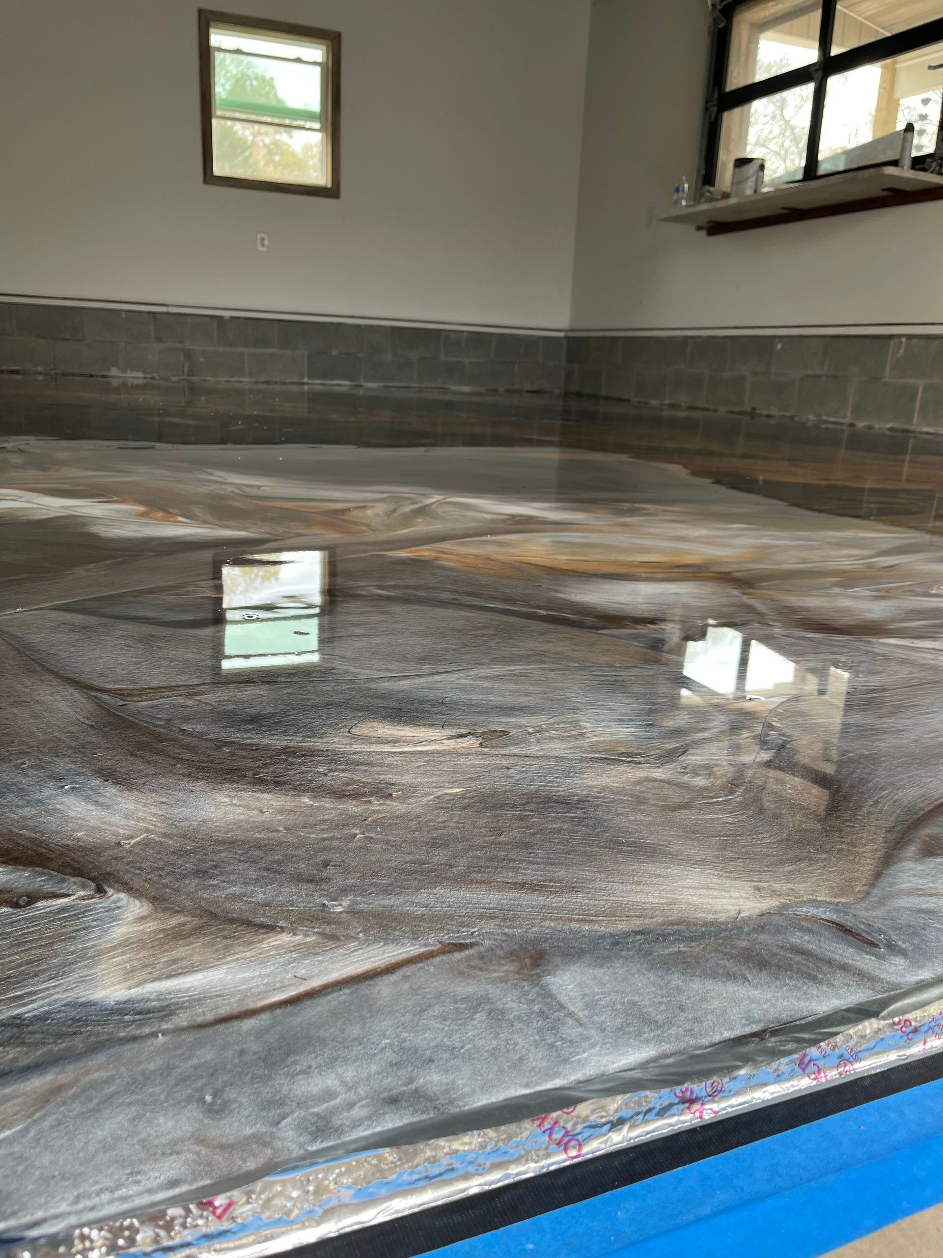 Water pooled on a blue tarp inside an empty room with tiled walls and windows.