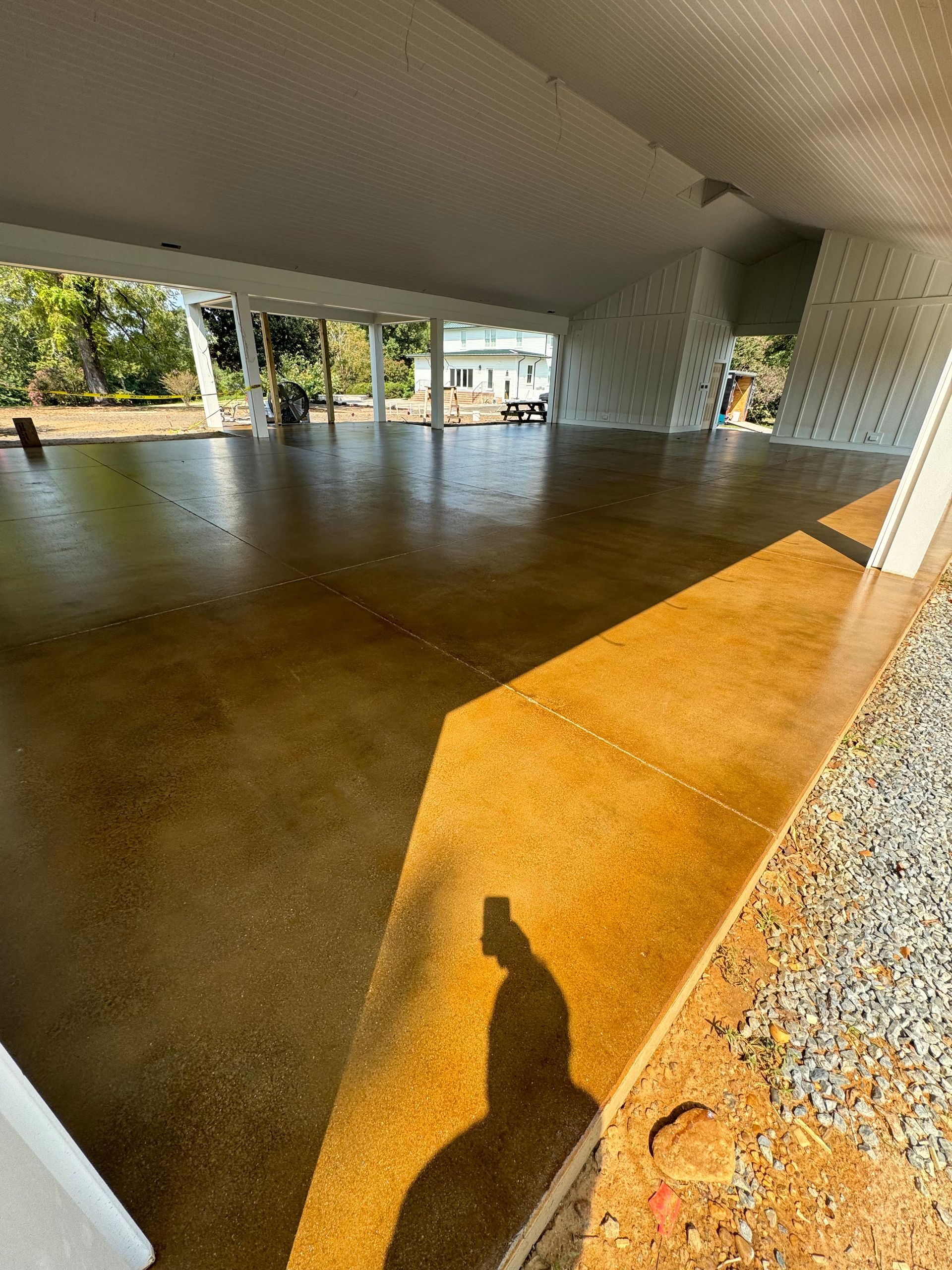 Empty covered outdoor patio with polished concrete floor and white columns, sunlight casting long shadows.