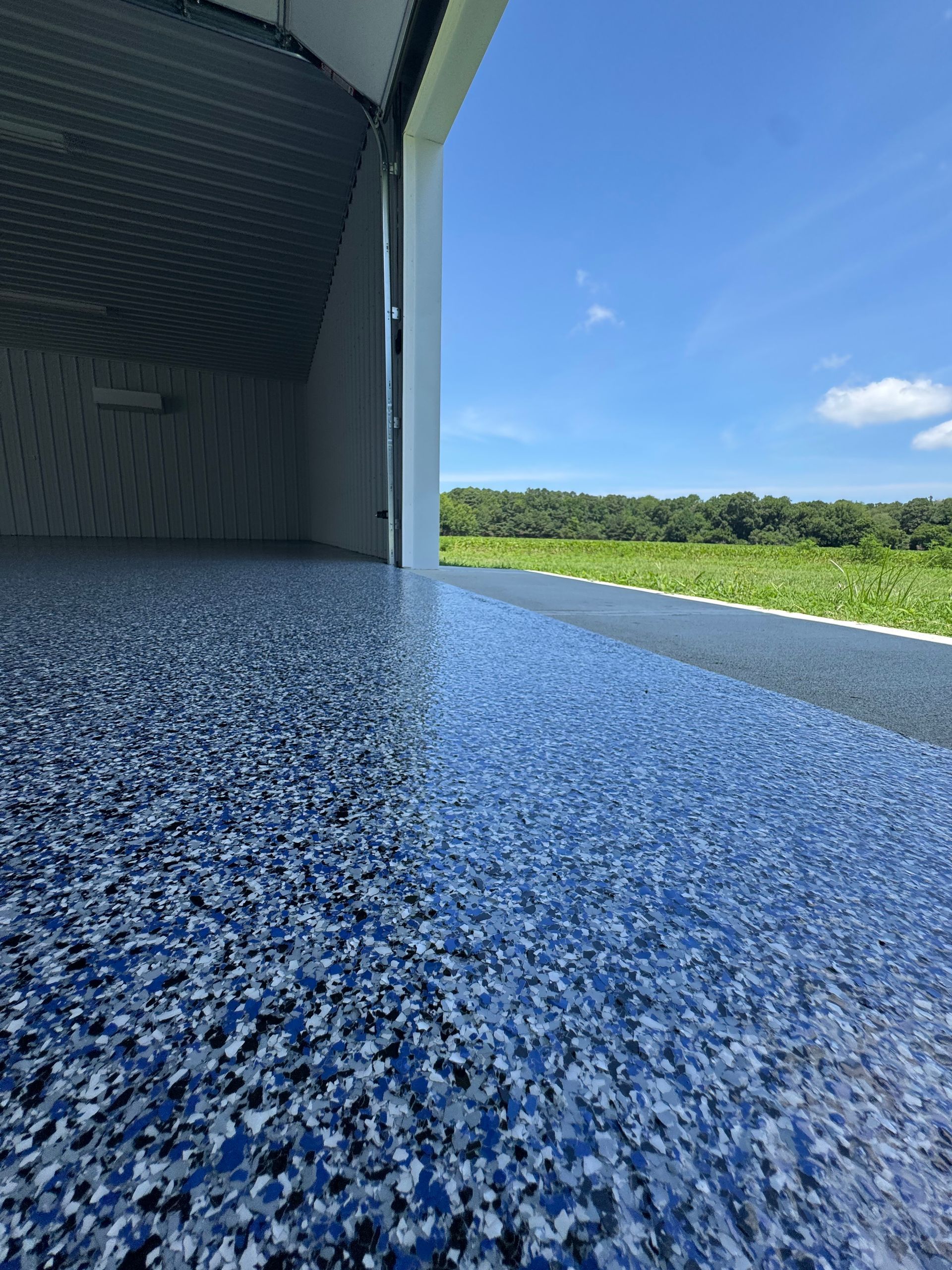 Blue speckled surface by an open hangar, overlooking a green field under a bright sky.
