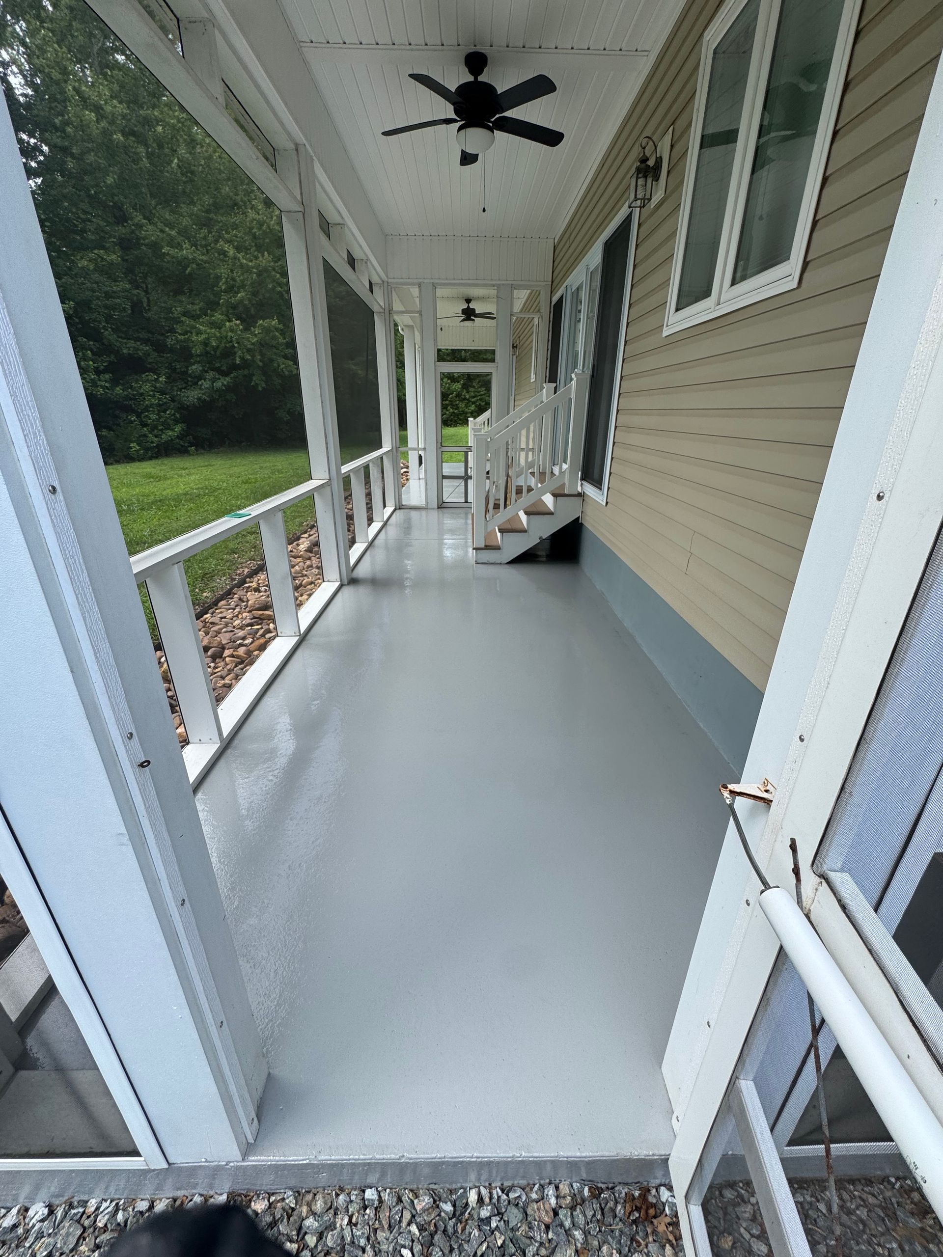 Covered front porch with white railing, gray floor, ceiling fan, and beige house siding.