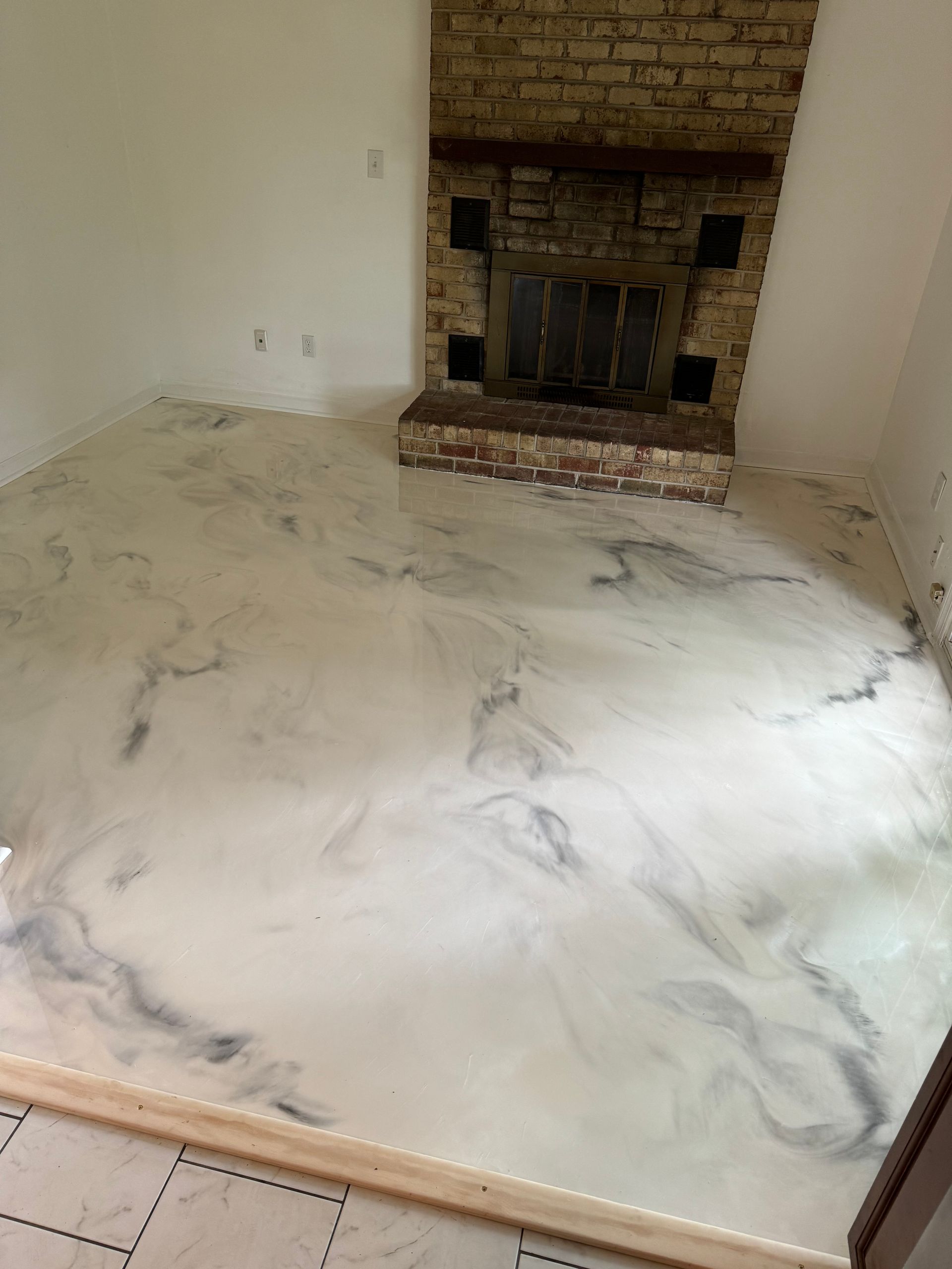 Empty living room with a brick fireplace and white marbled floor, viewed from a doorway.