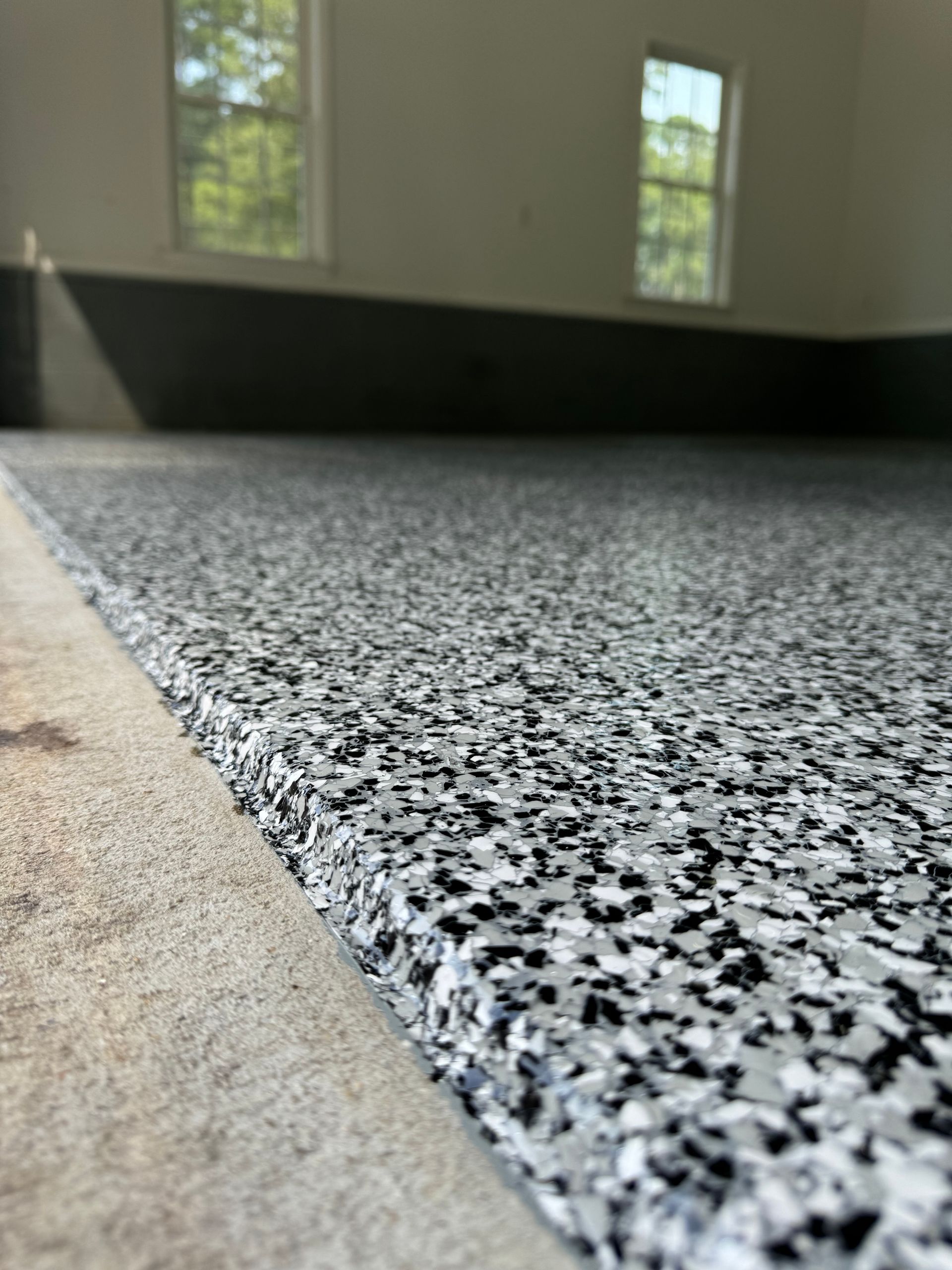 Black-and-white speckled floor edge with beige trim in an empty room near windows