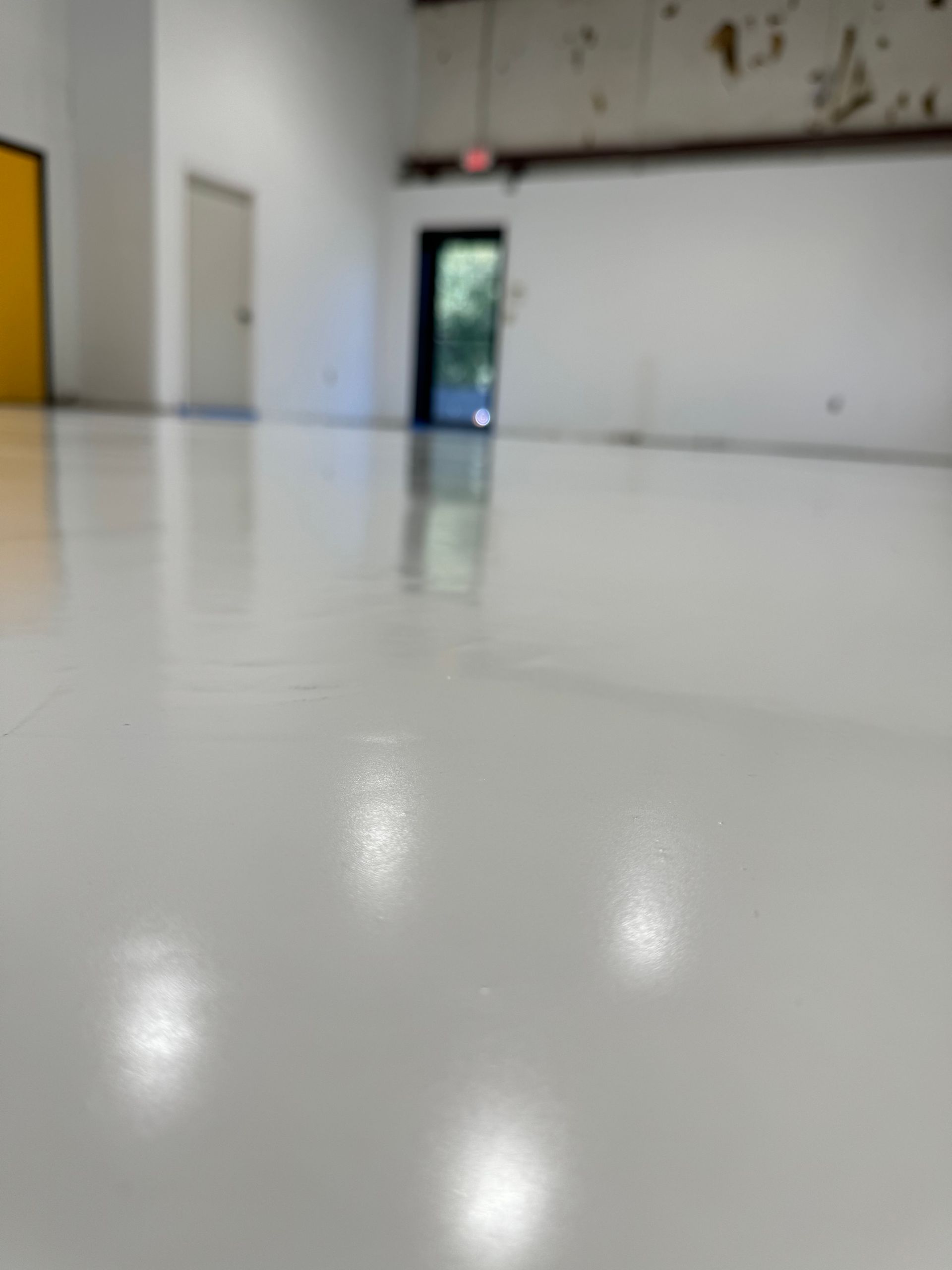 Empty white indoor room with glossy floor, a closed door, and an open doorway at the back.