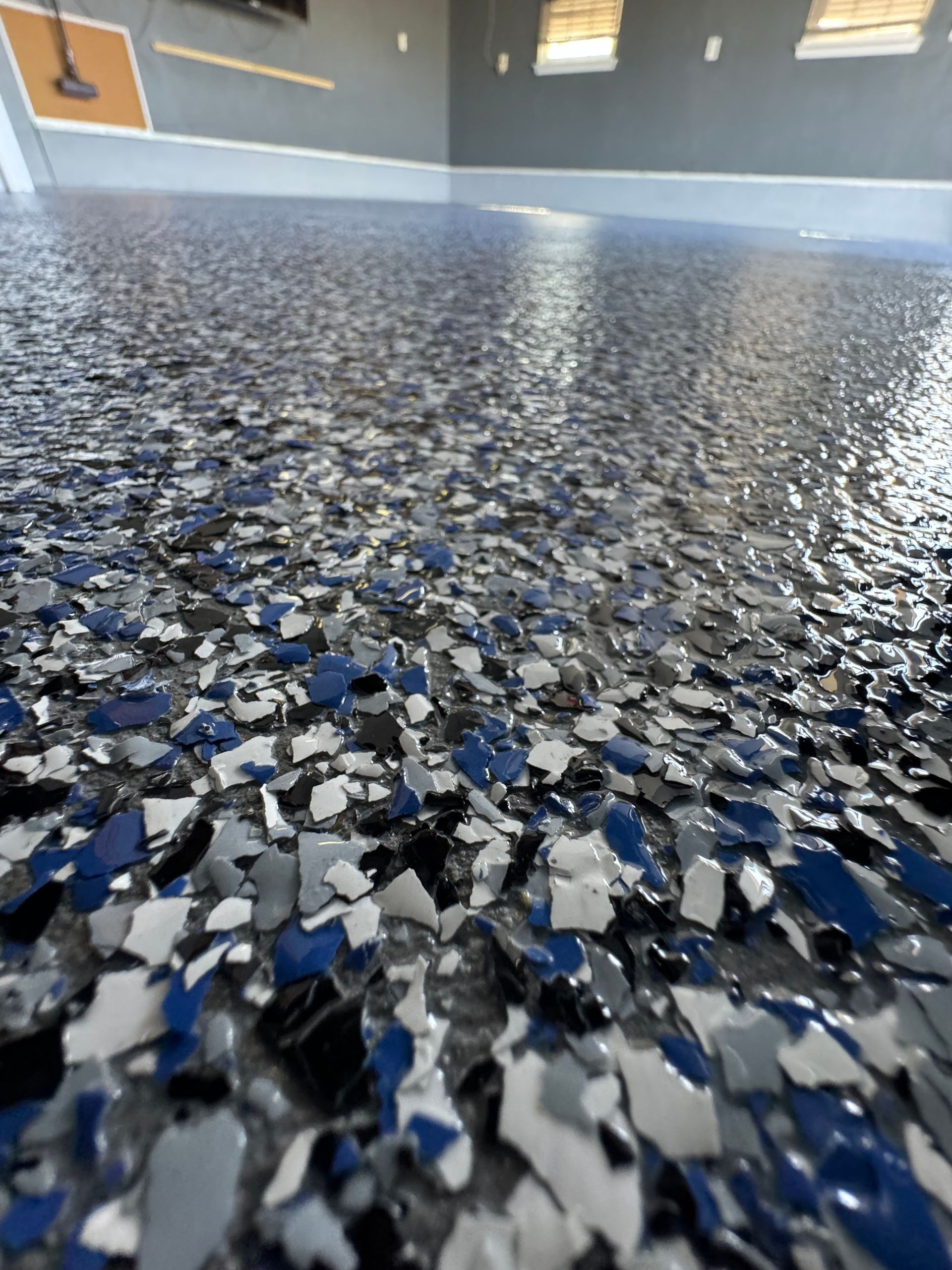 Close-up of speckled blue, gray, and white epoxy floor with a glossy surface and blurred wall in the background