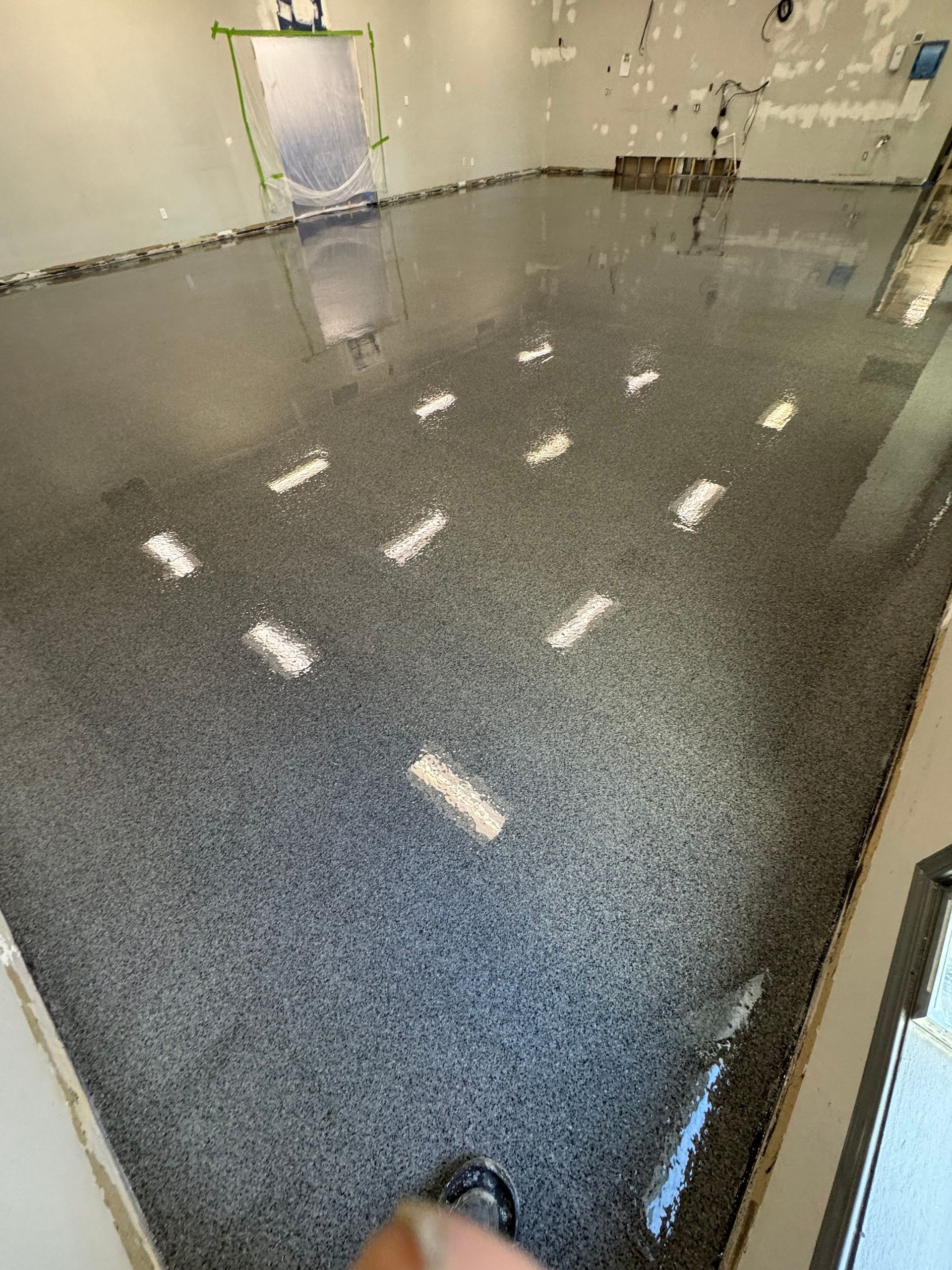 Glossy gray speckled floor in an empty room with reflections and a door in the back