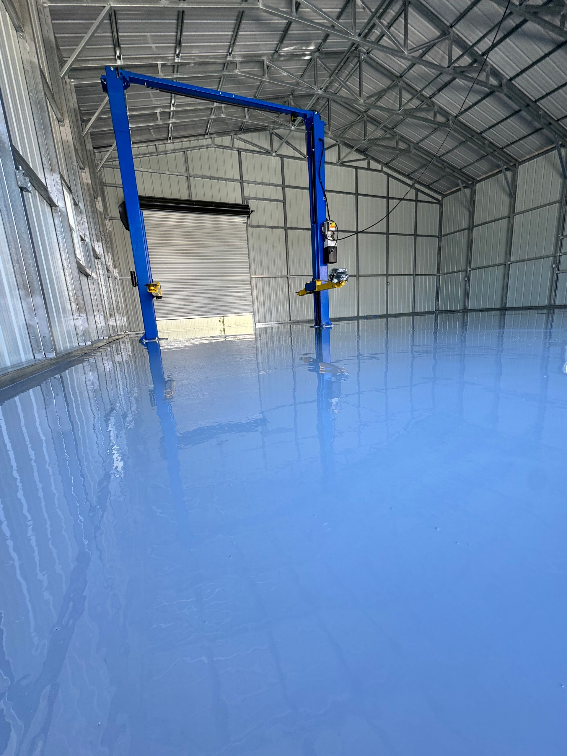Blue resin floor inside a large industrial warehouse with metal walls and ceiling framing.