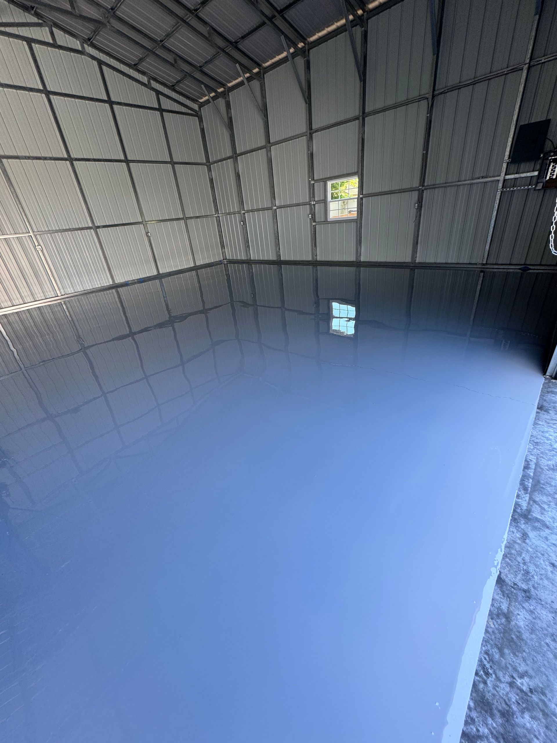 Empty insulated room with gray walls and a glossy blue floor, lit by a small window.