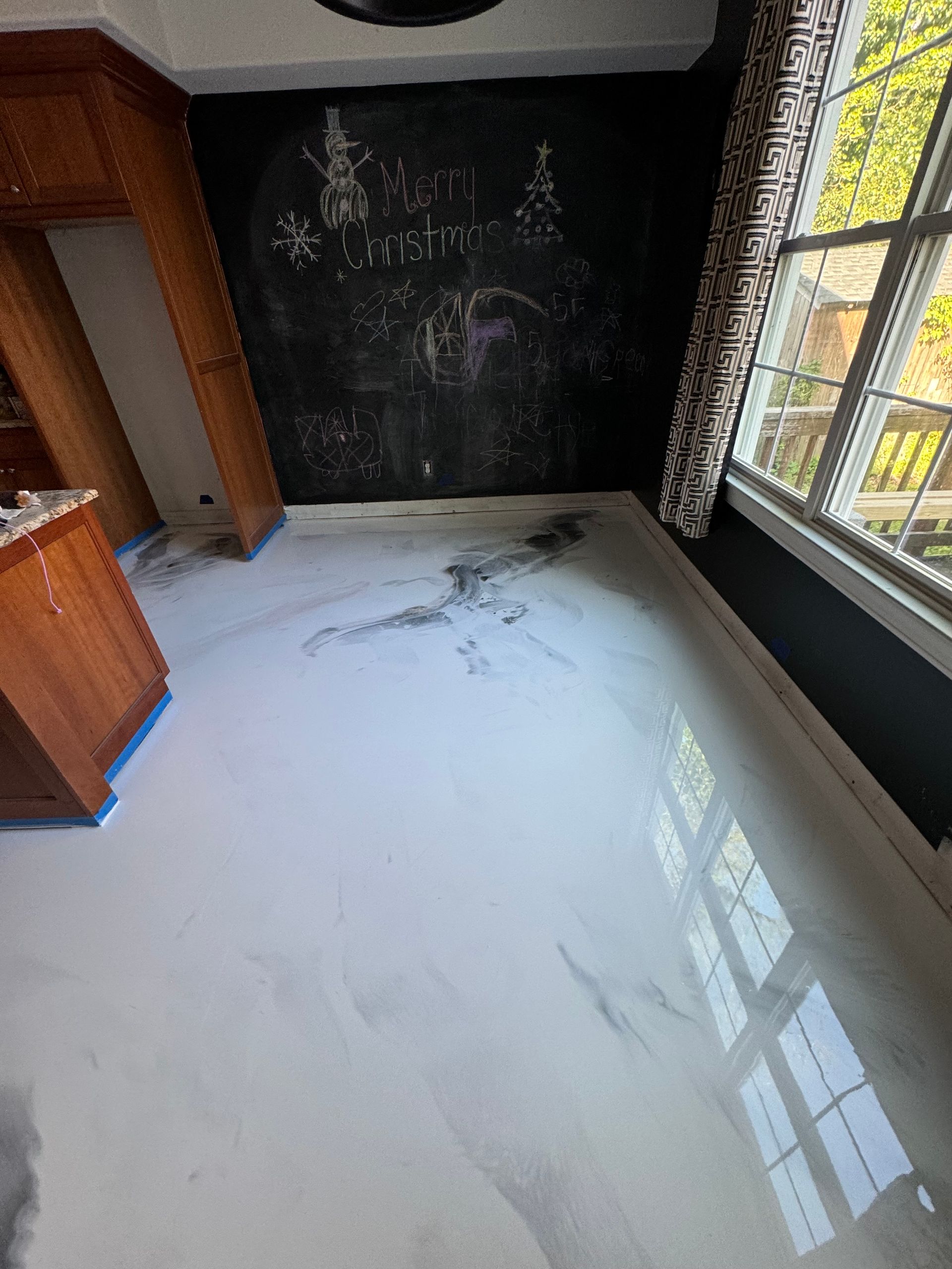 Empty room with glossy white floor, black chalkboard wall, and large window letting in daylight