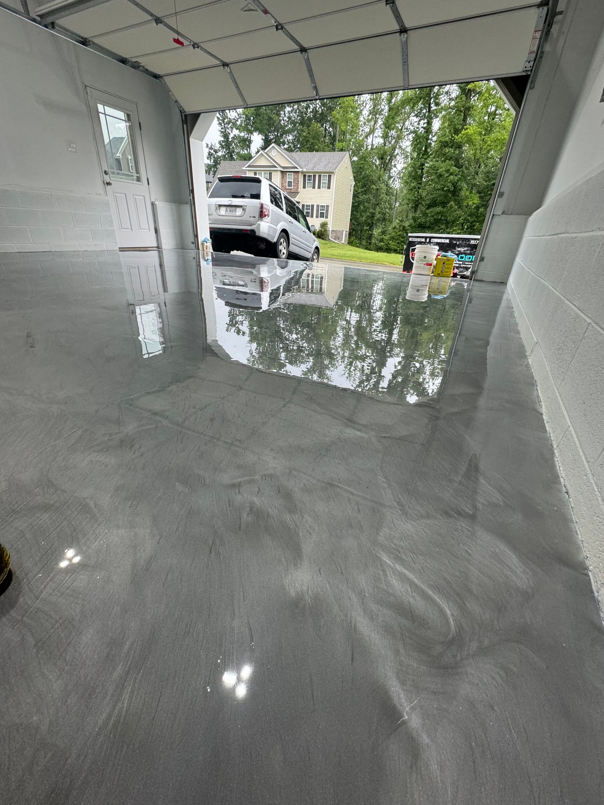 Covered driveway with glossy wet floor, a white van outside, and trees visible beyond.