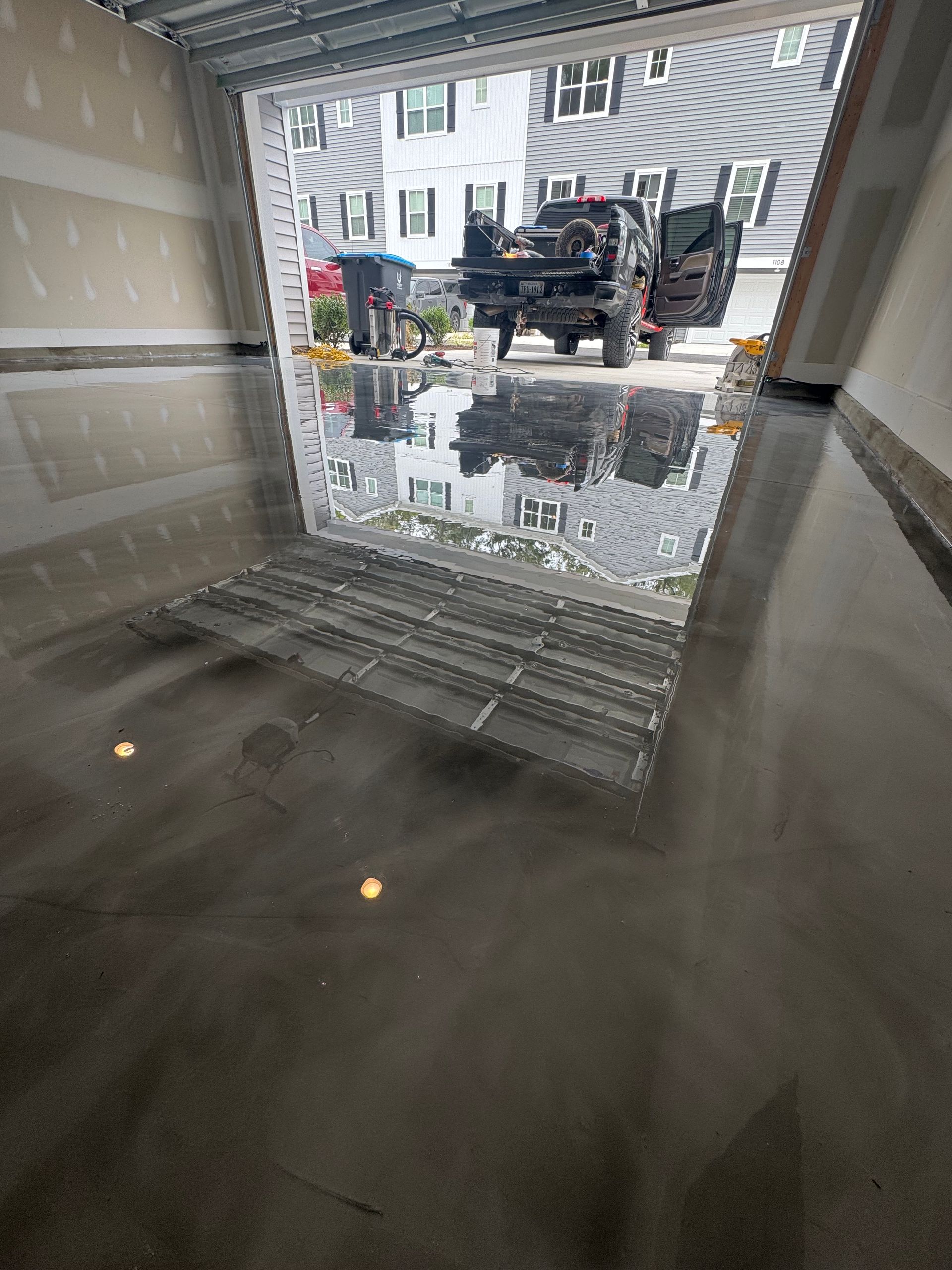 Flooded garage with water reflecting the open entrance and parked vehicles outside.