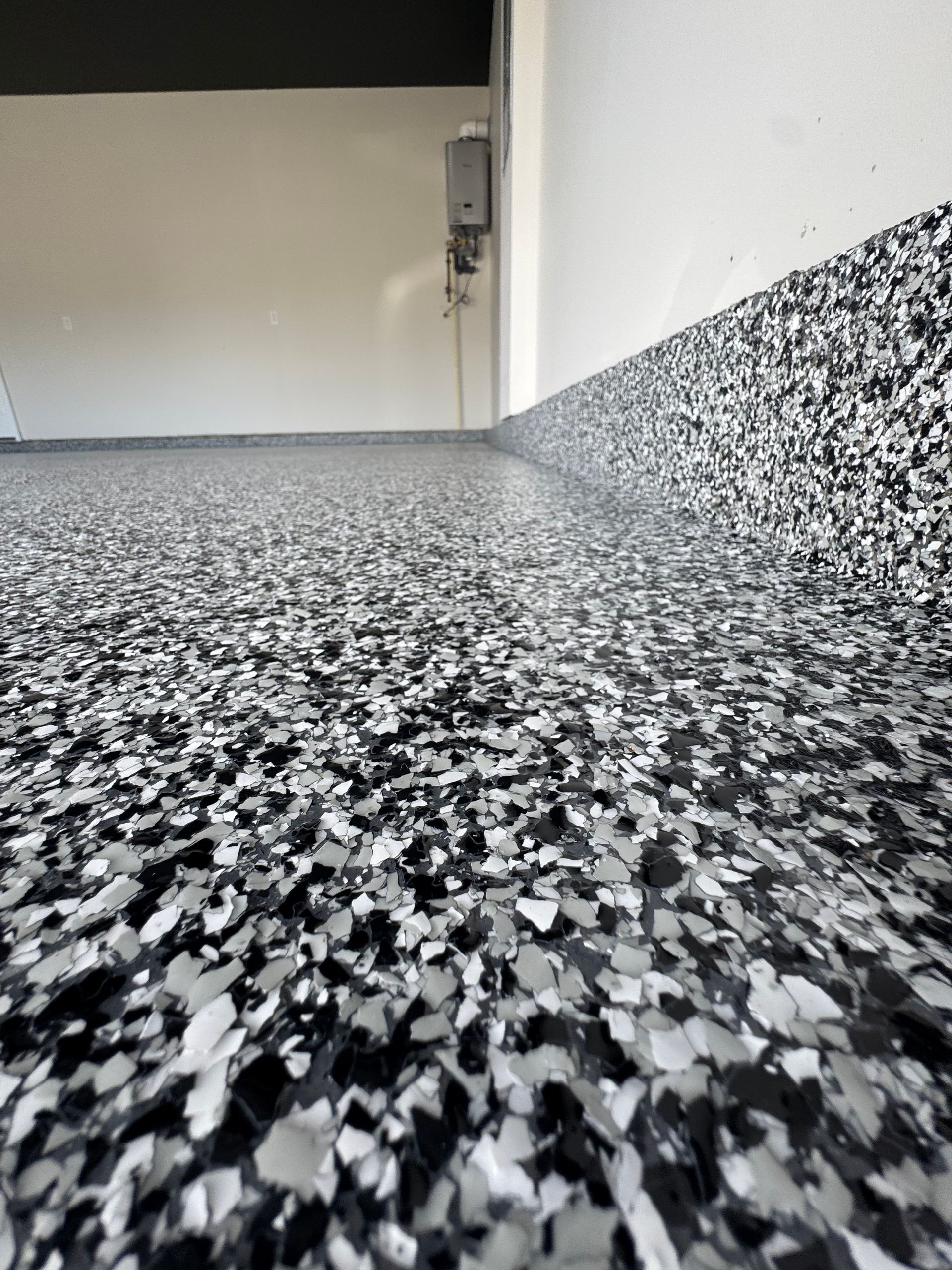 Close-up of speckled black, white, and gray floor leading to a white wall and open doorway.