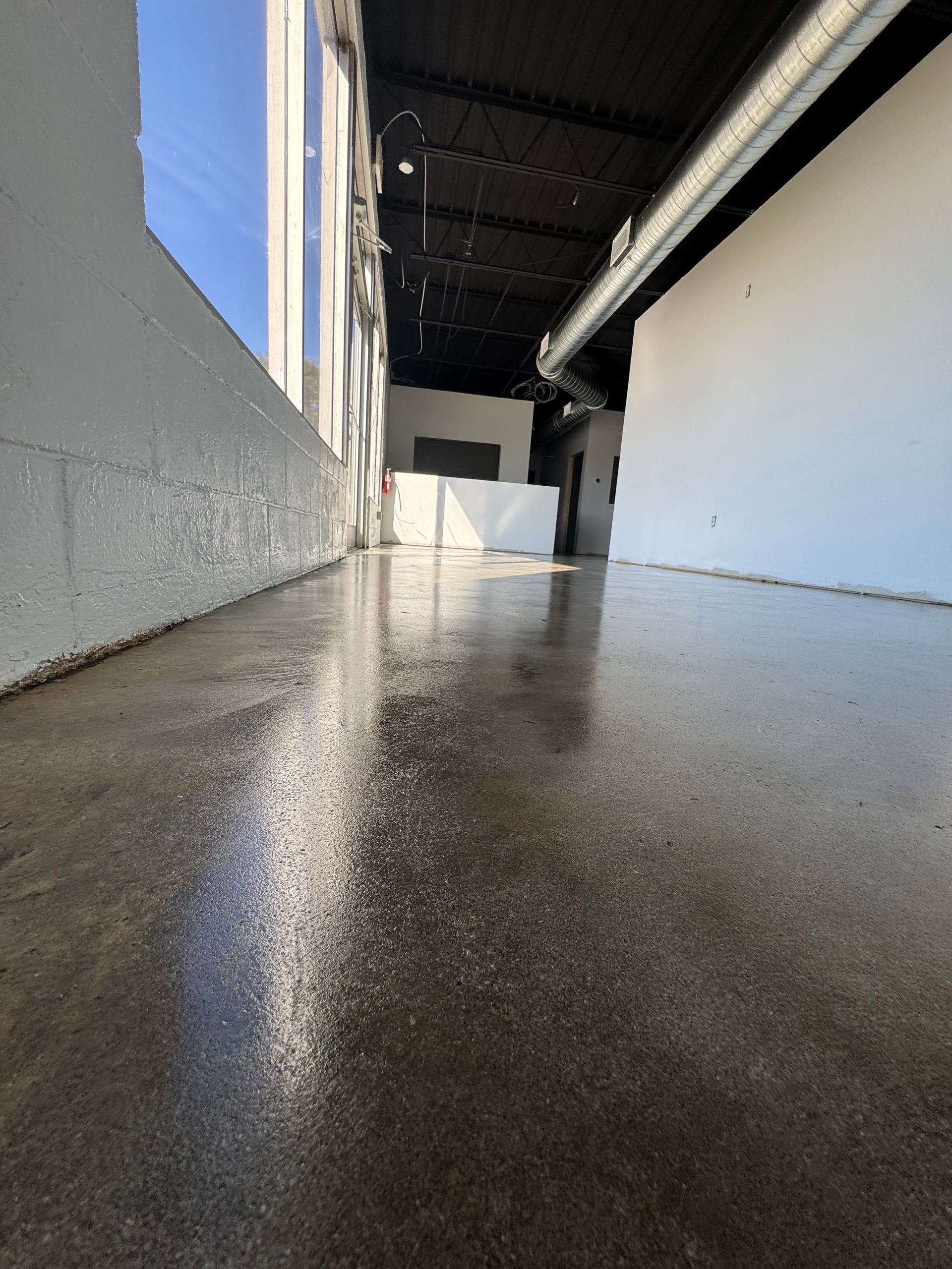 Wet concrete walkway beside a building, with a covered passage and blue sky at left