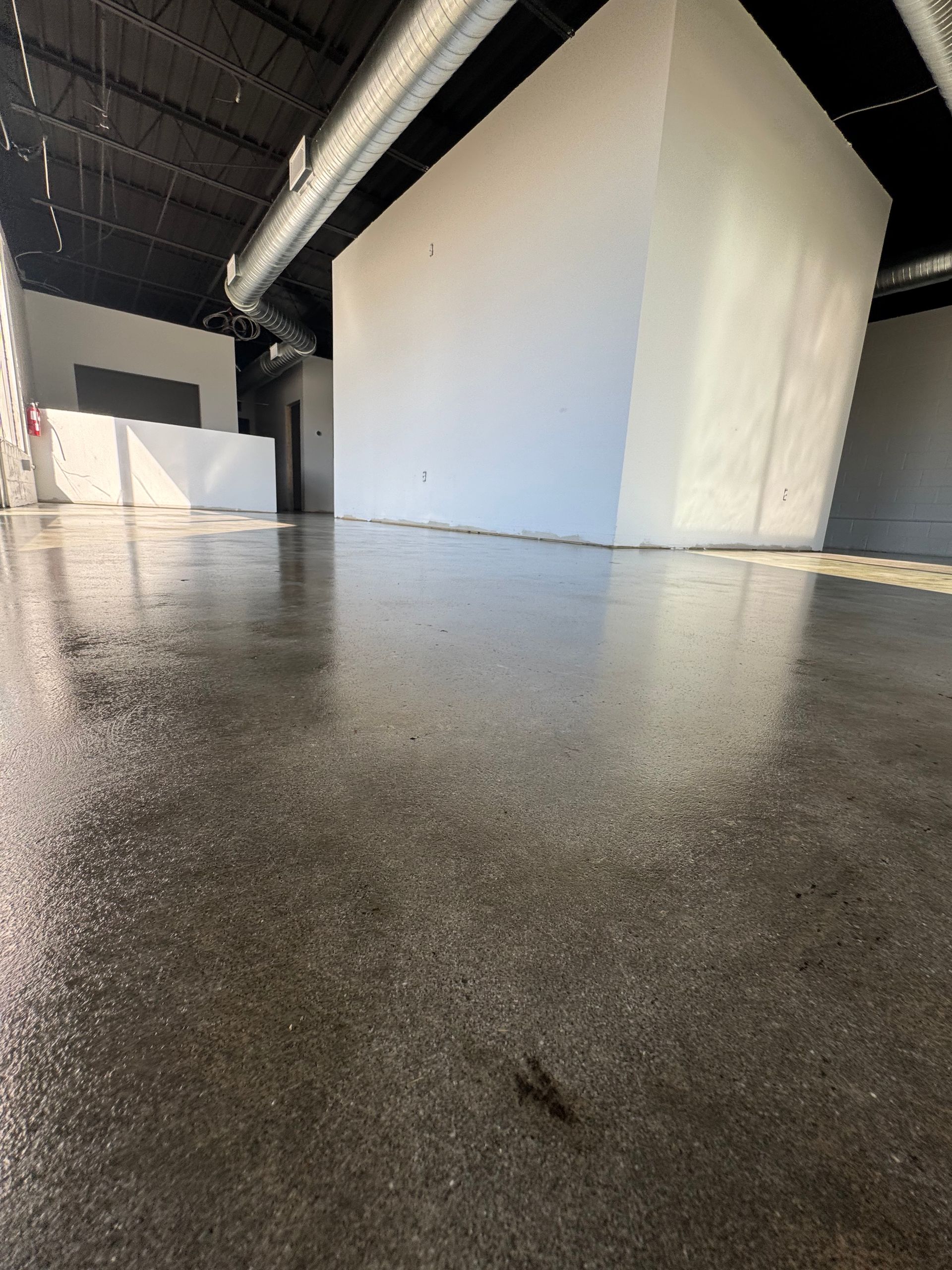 Empty industrial hallway with a glossy concrete floor and large white wall panels under overhead ducting