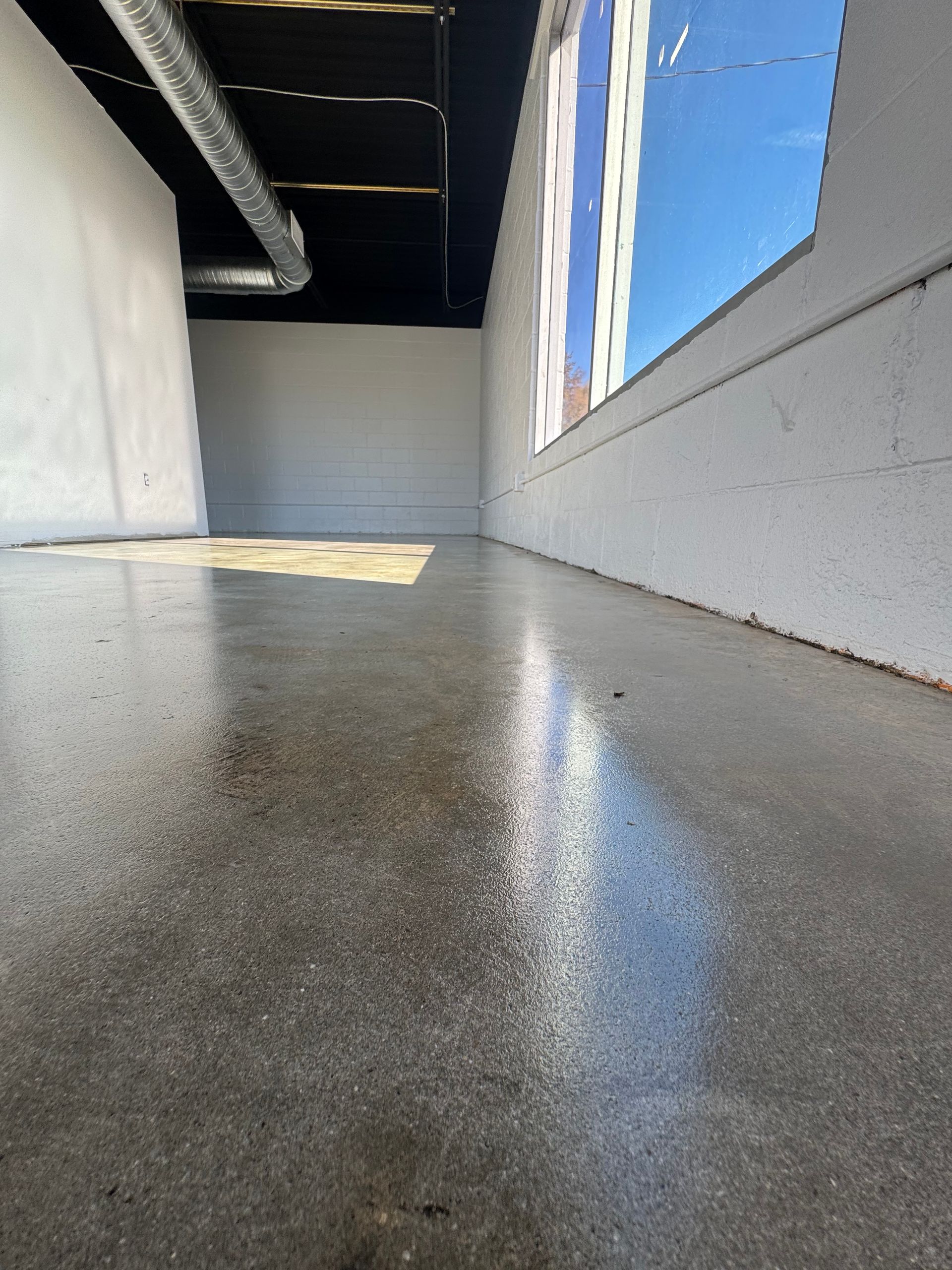 Low-angle view of an empty corridor with gray floor, white walls, and a blue sky visible through windows