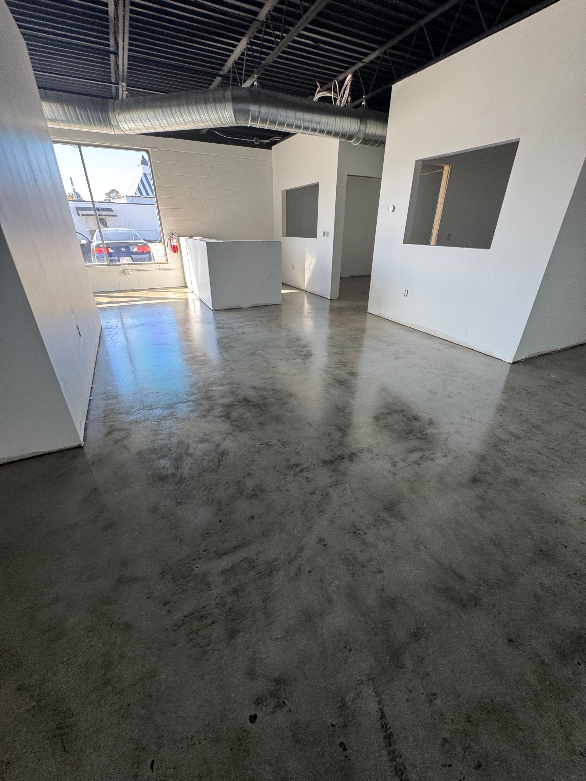 Empty unfinished room with polished concrete floor, white walls, and an open doorway to the outside.