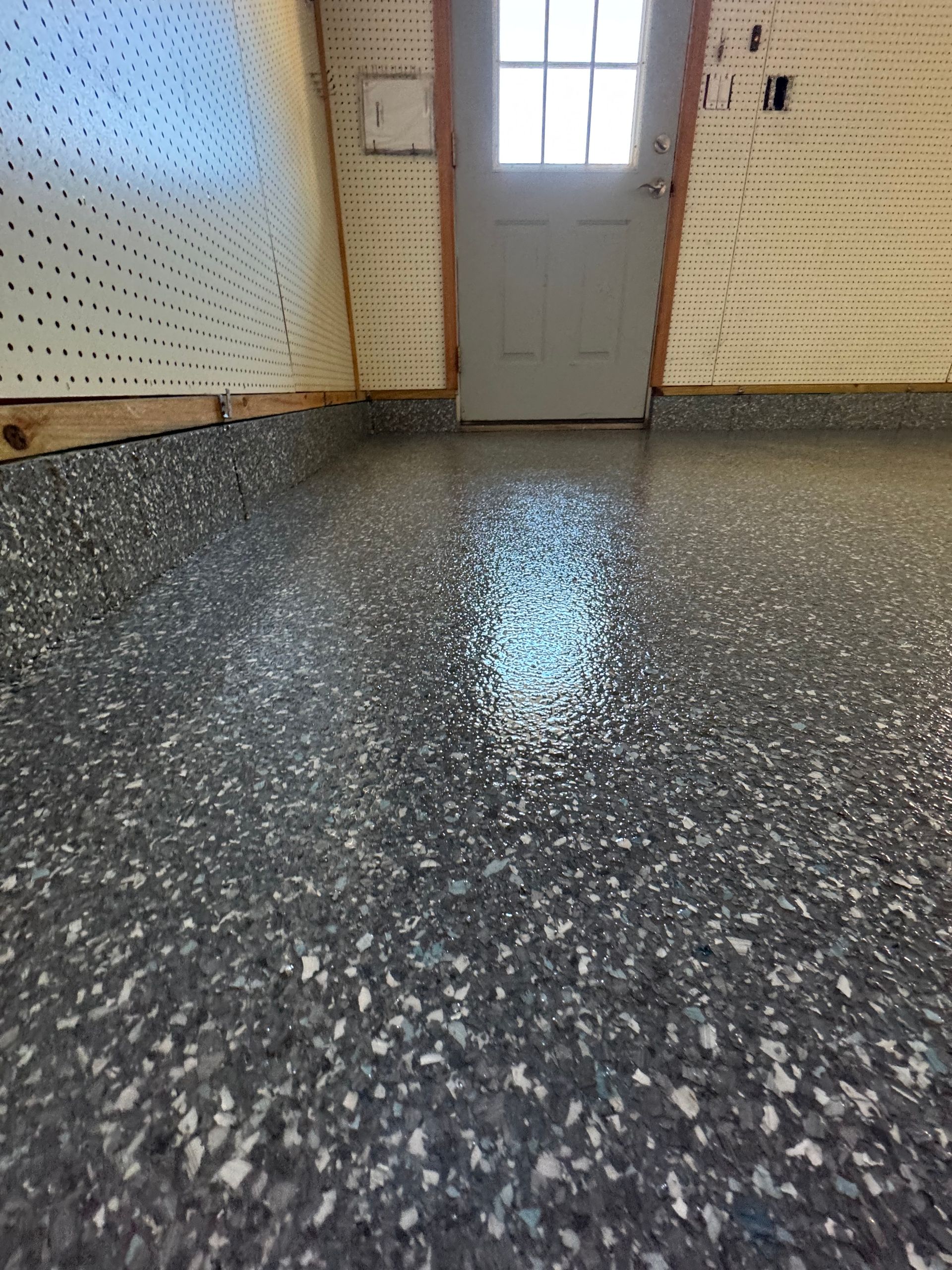Empty room with speckled gray floor, beige walls, and a closed door with a window.