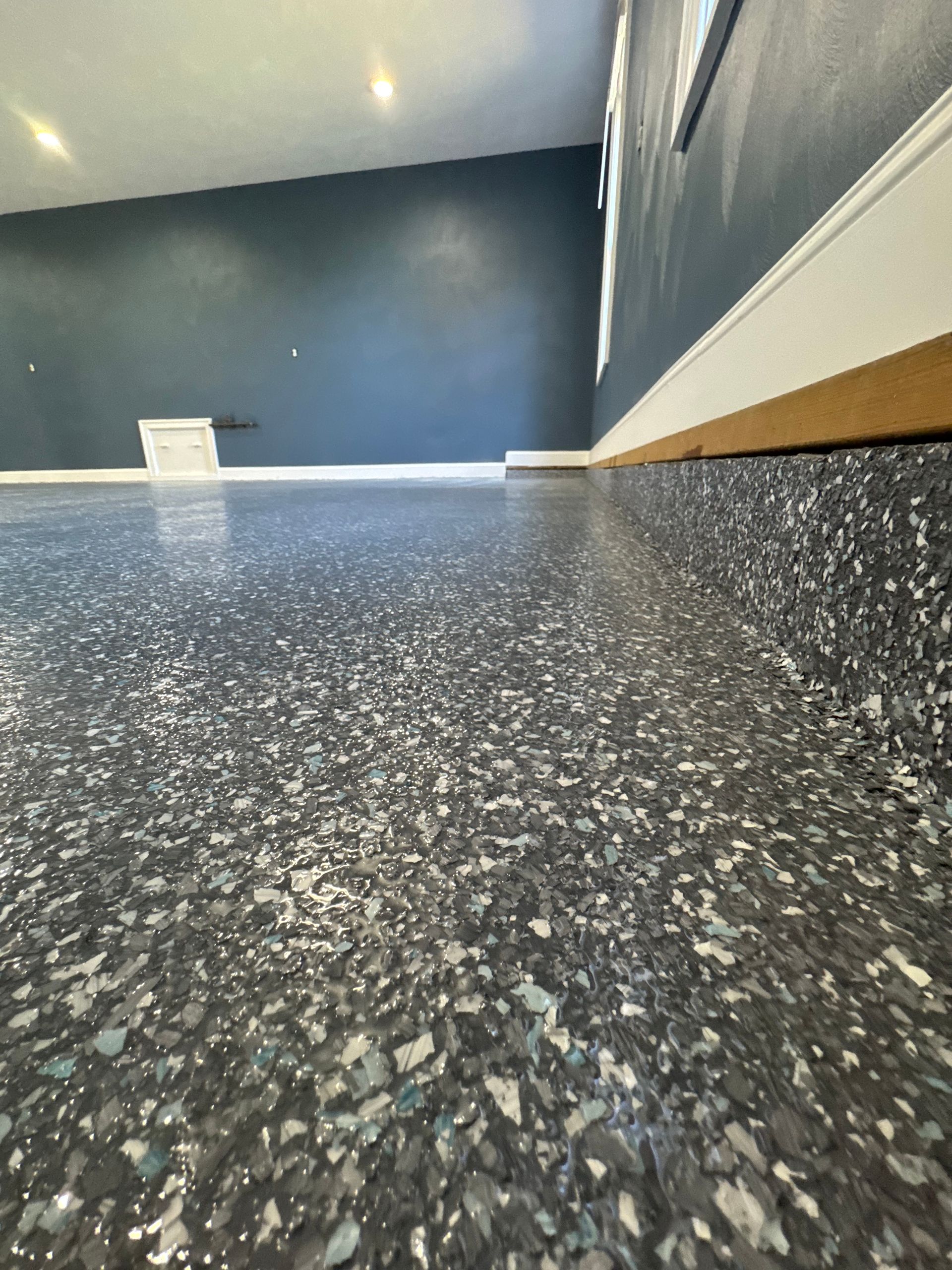 Low-angle view of a blue-walled room with a speckled black floor and white trim.