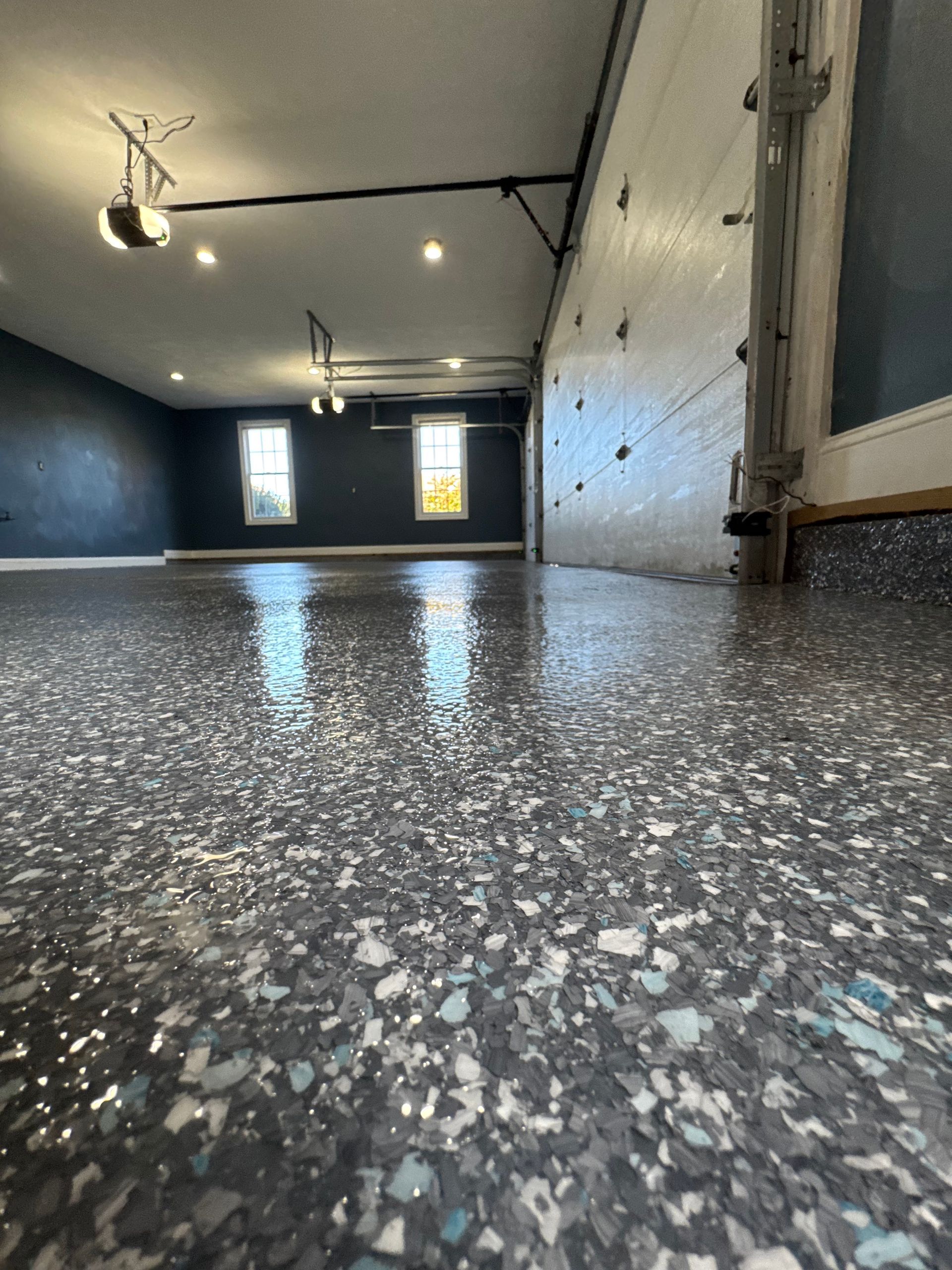 Empty garage with speckled epoxy floor, dark walls, ceiling lights, and two small windows.