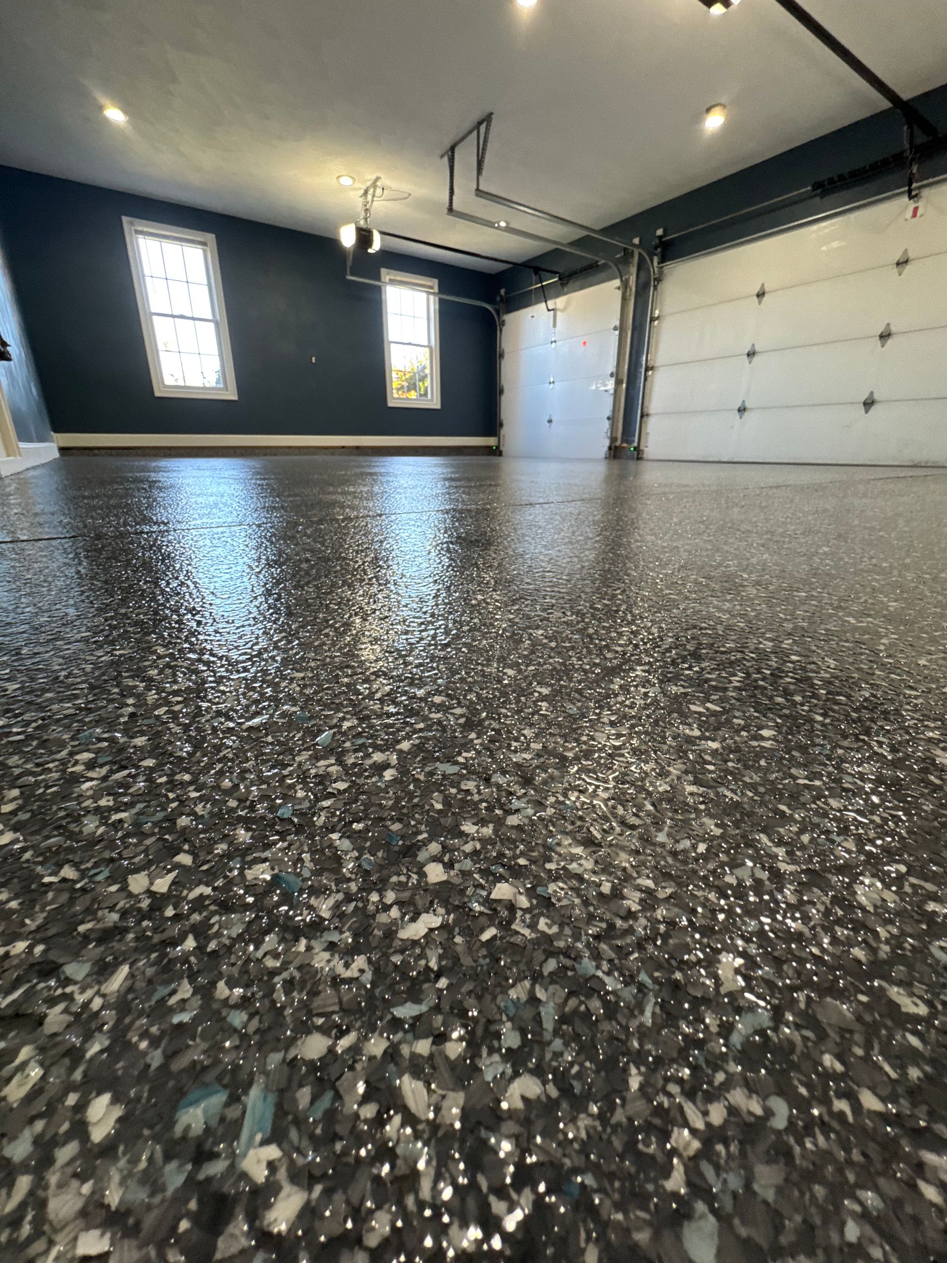 Empty garage interior with speckled epoxy floor, white overhead door, and two small windows.