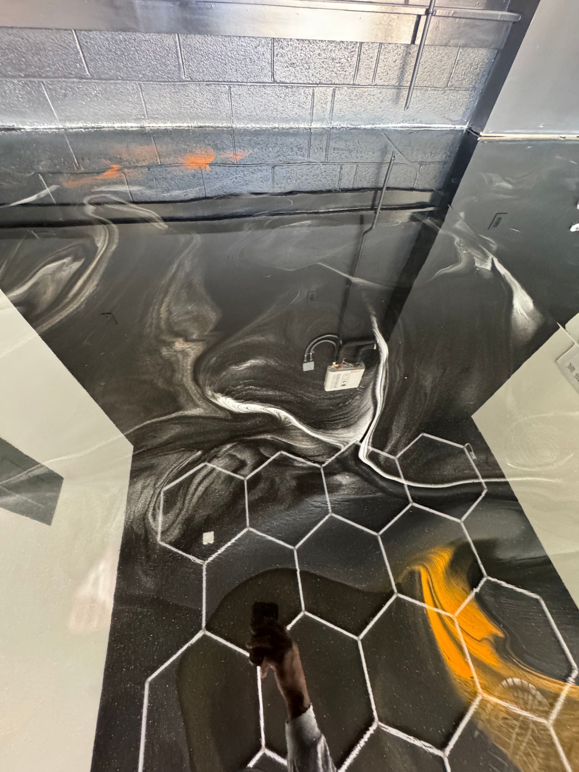 Black-and-white abstract mural with hexagonal floor pattern and orange accents in an indoor hallway