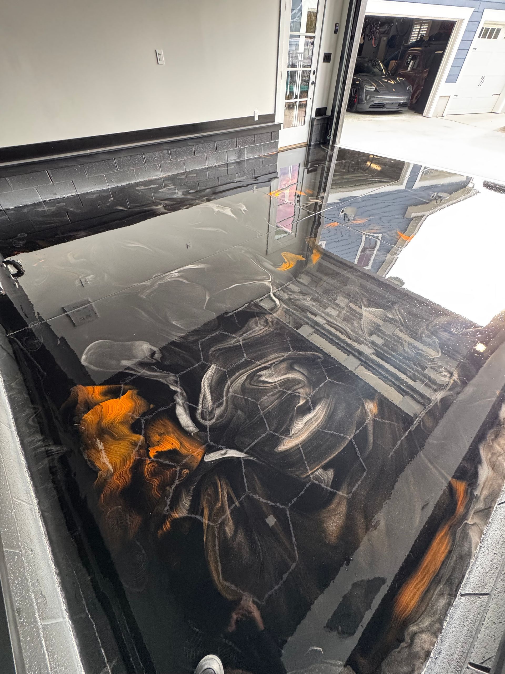 Burned black car interior with melted dashboard and orange flames, parked inside a garage