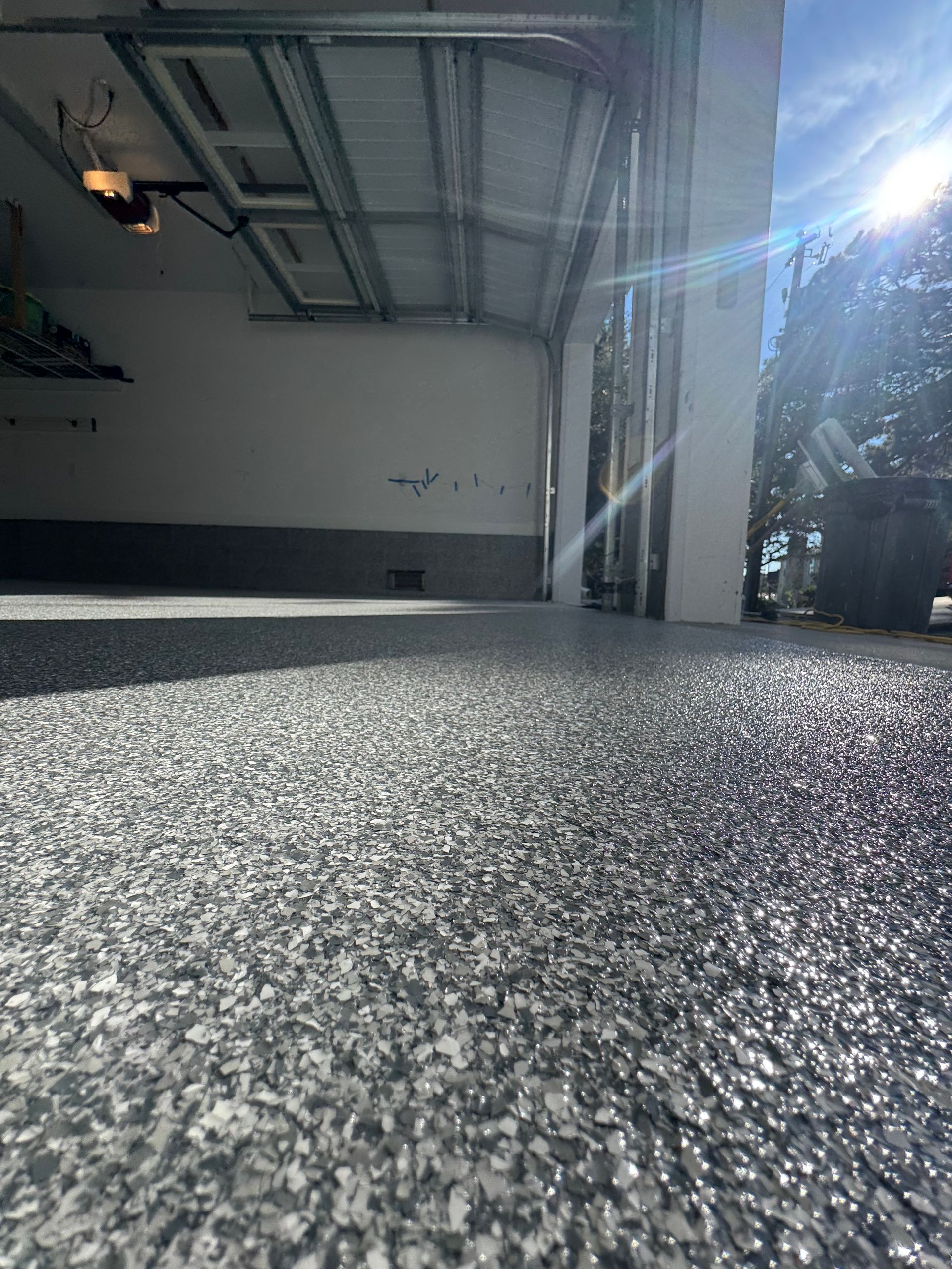 Low-angle view of a garage interior with sunlight streaming through the open door onto a textured floor.