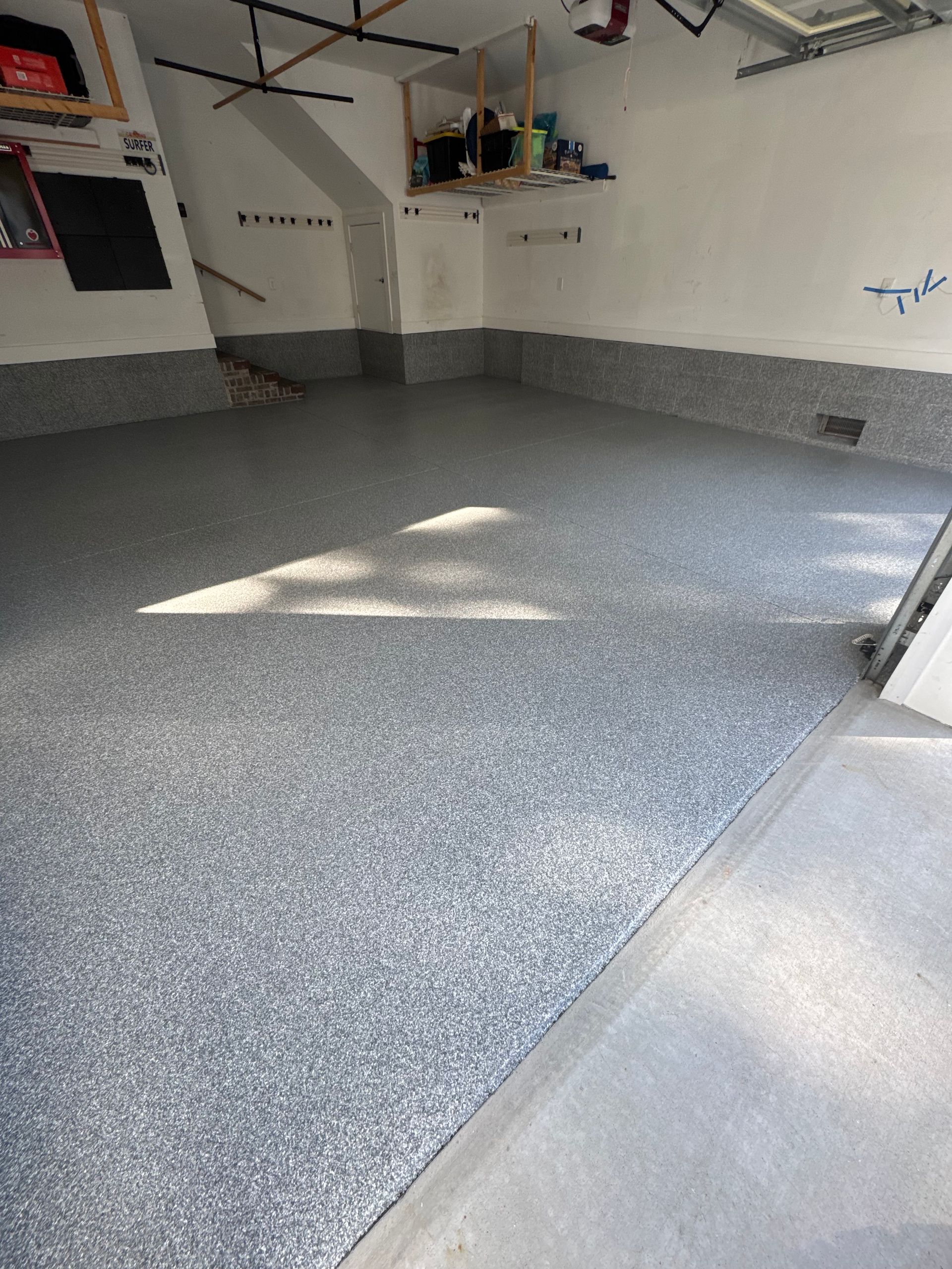 Empty garage with gray speckled epoxy floor and white walls, lit by sunlight from the open door