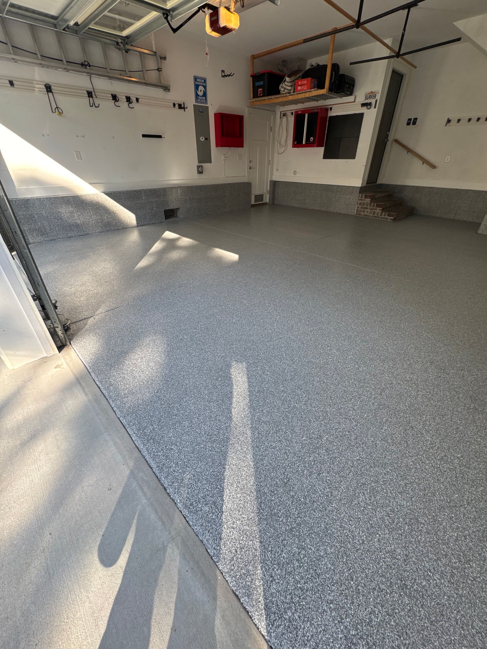 Empty garage with speckled gray epoxy floor, white walls, red cabinets, and sunlight streaming in