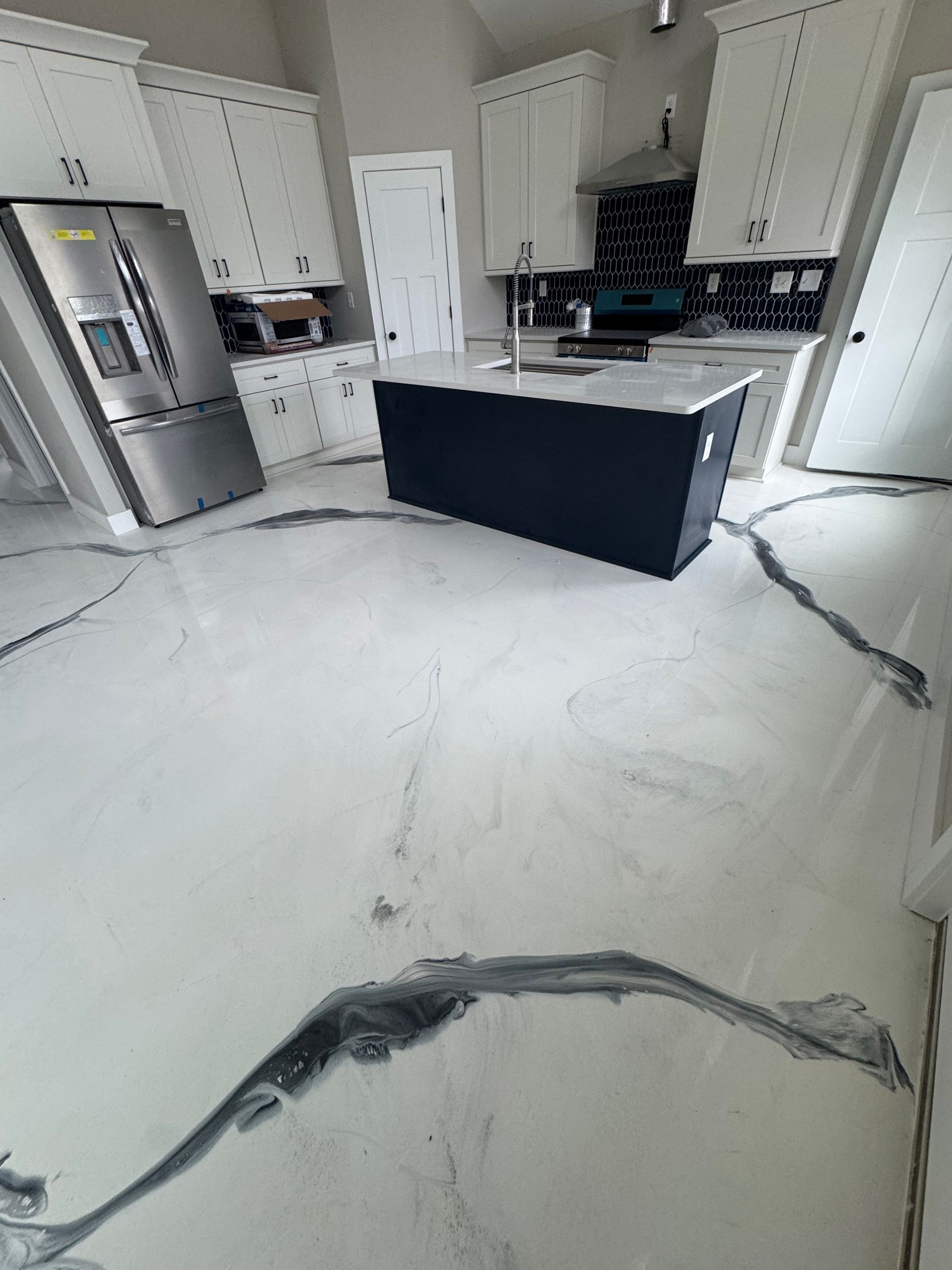 Modern kitchen with white cabinets, stainless fridge, black island, and large white marble-pattern tile floor.