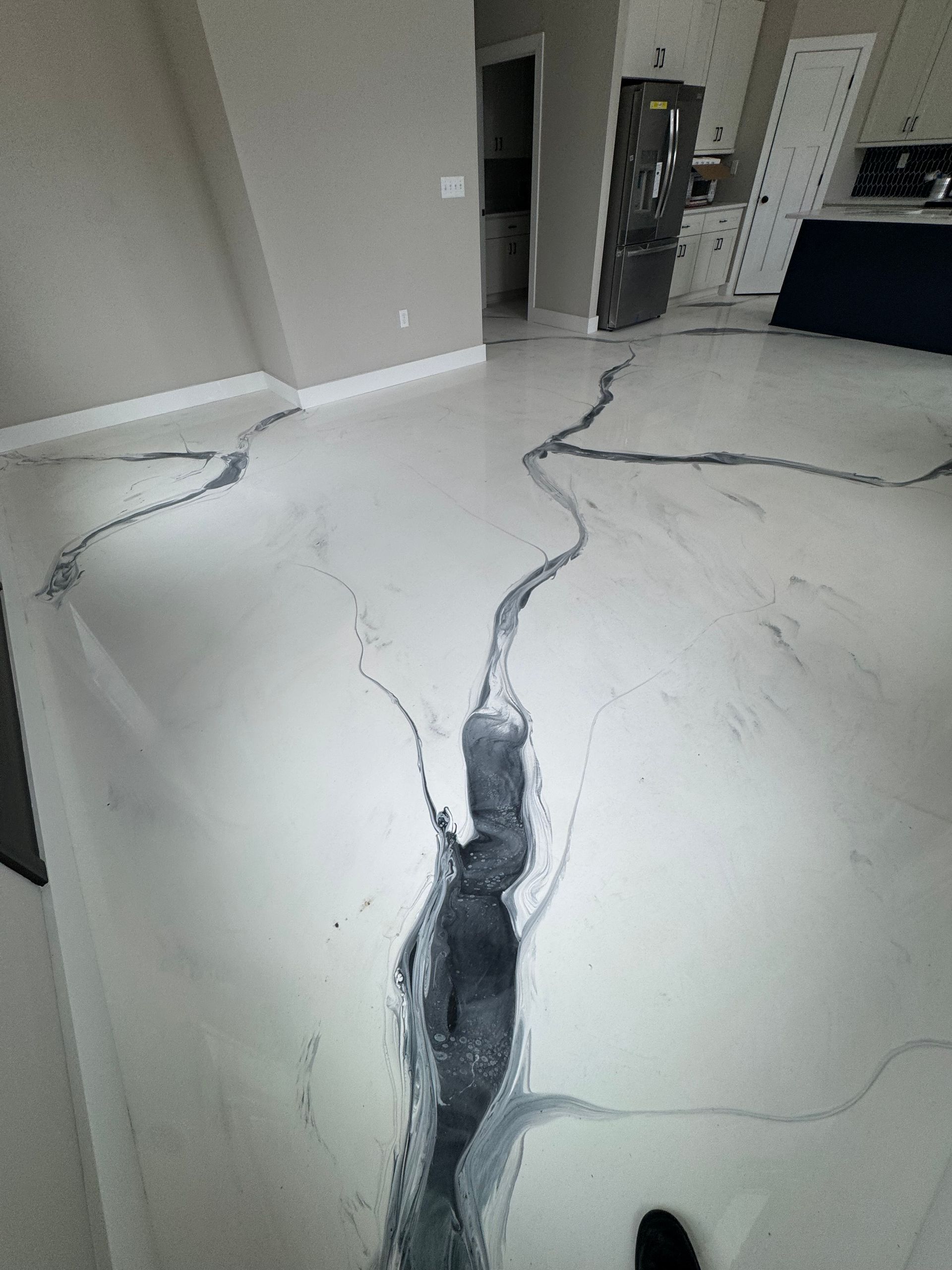 Cracked white floor with dark fissures in an empty room, leading toward a doorway.