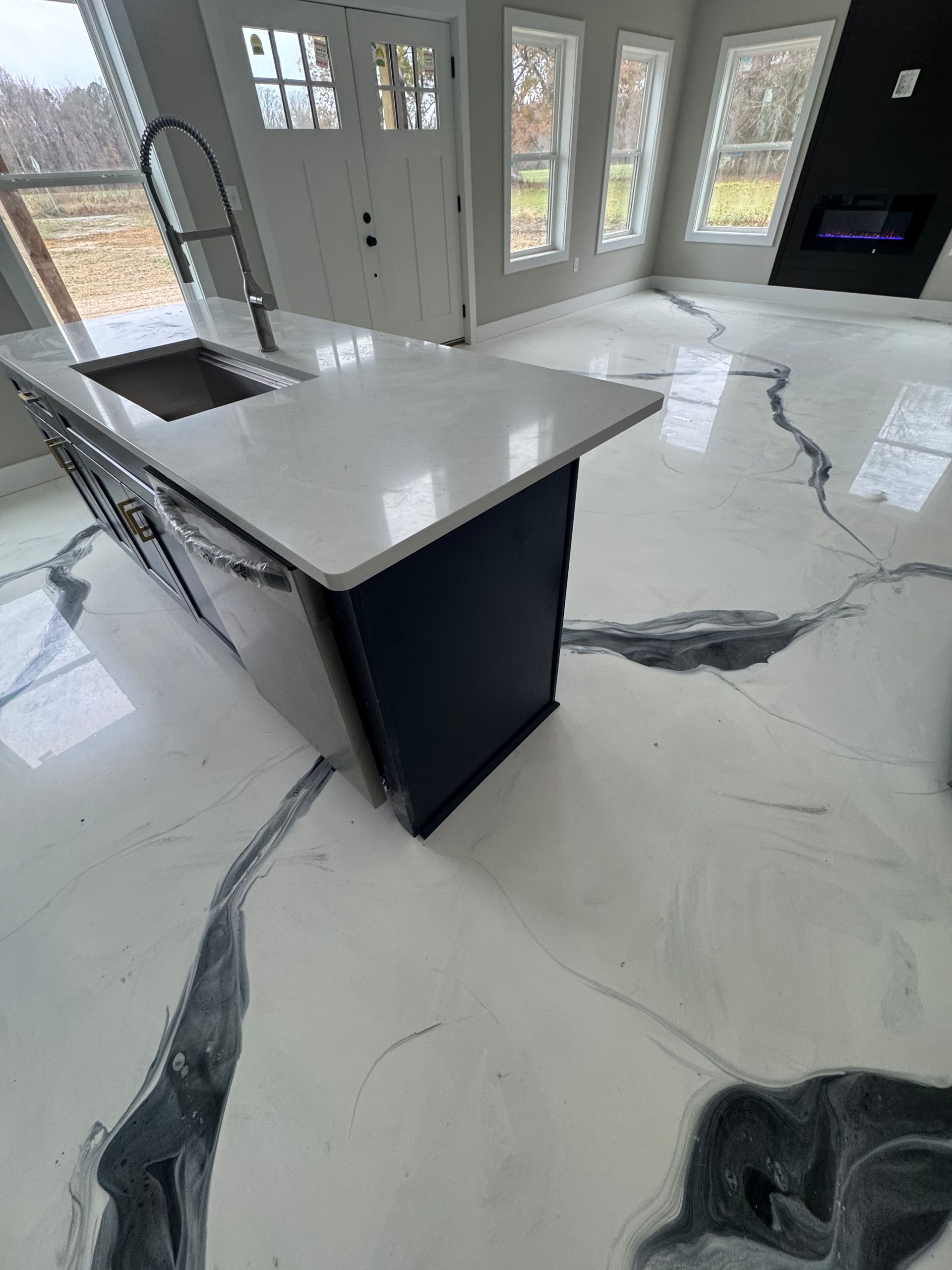 Modern kitchen with white island, glossy floor, and glass doors letting in daylight.