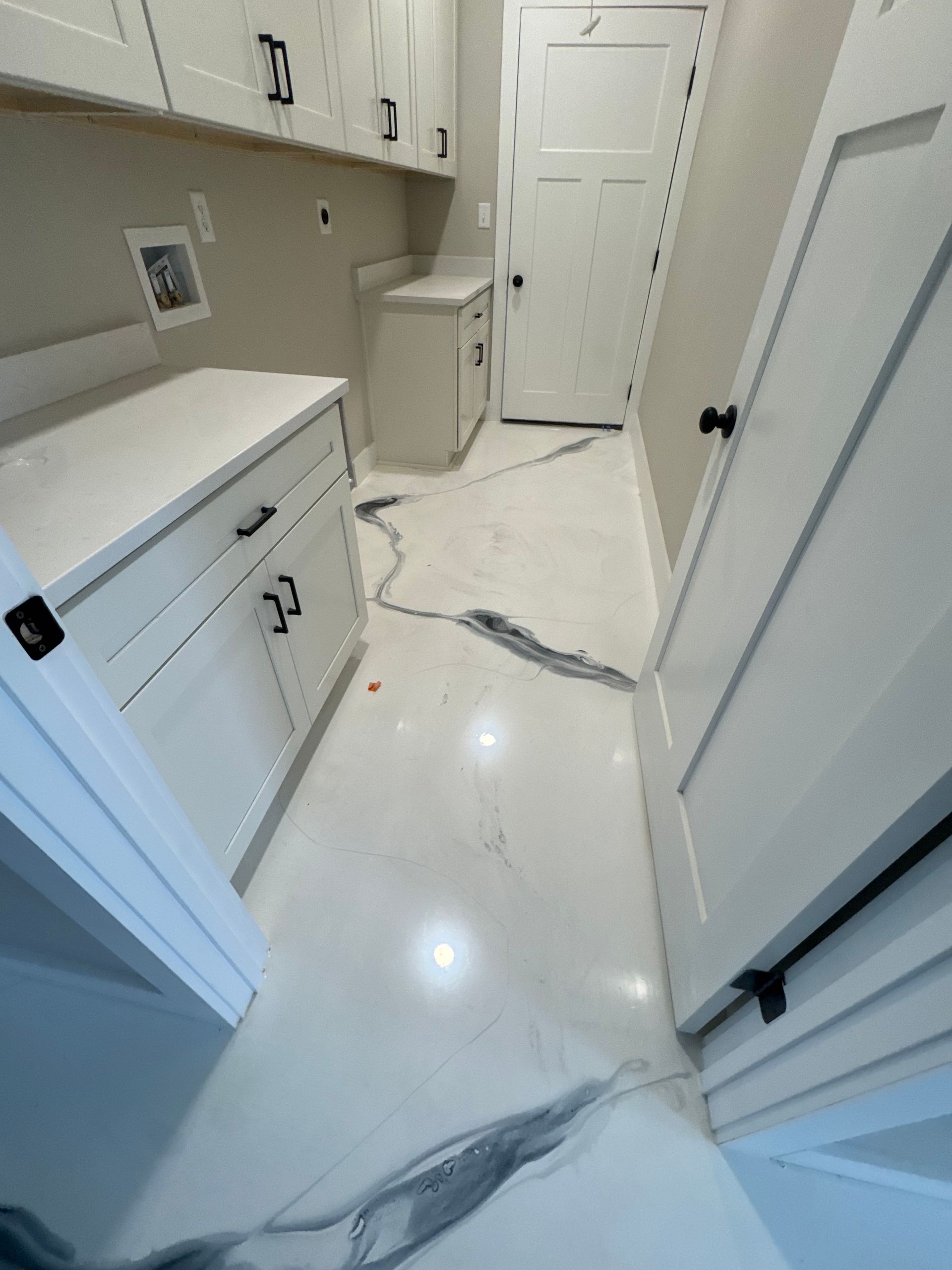 Modern laundry room with white cabinets, marble-patterned floor, and a sink by the door