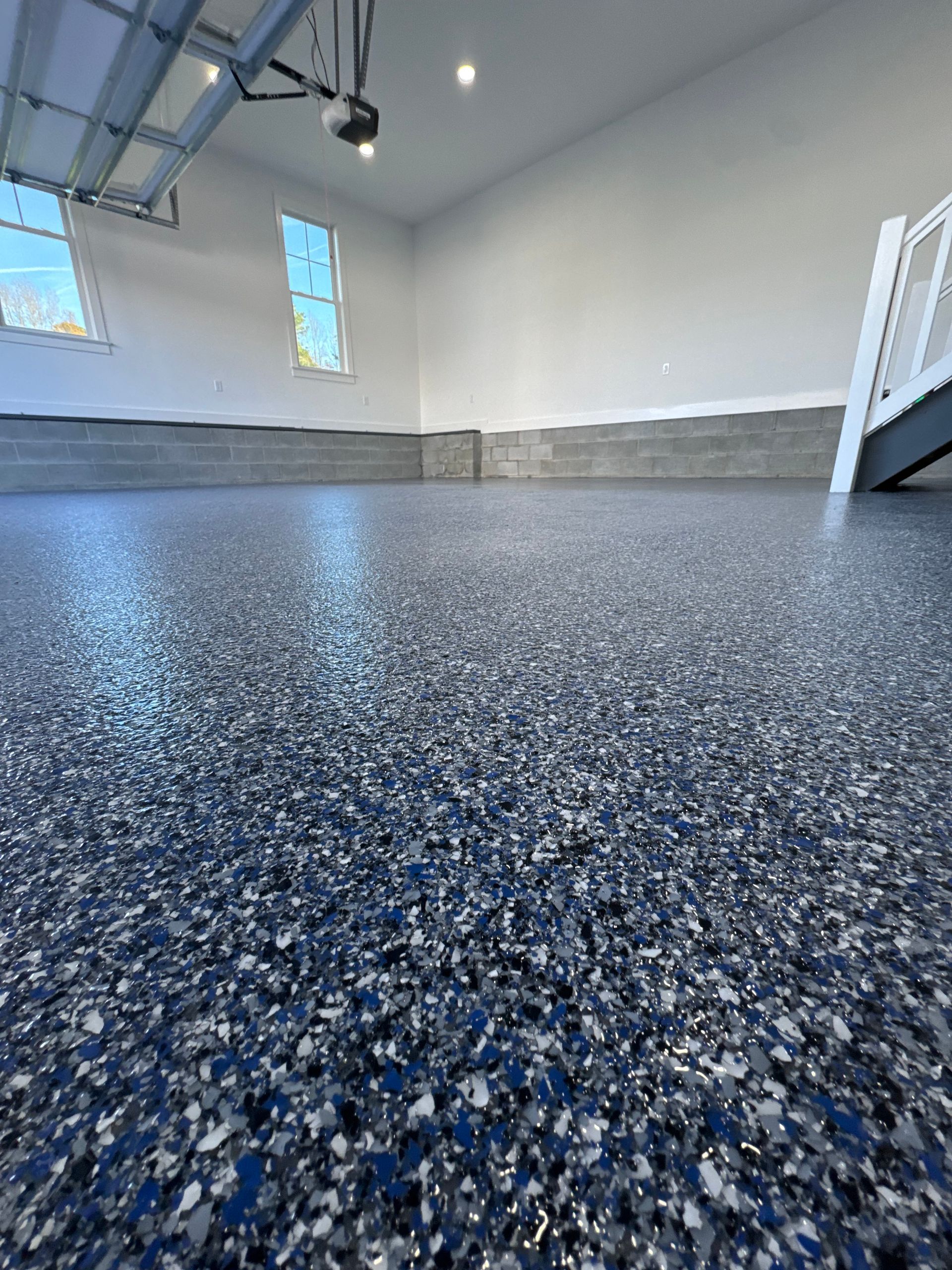 Empty garage with speckled blue epoxy floor and white walls, lit by daylight from small windows.