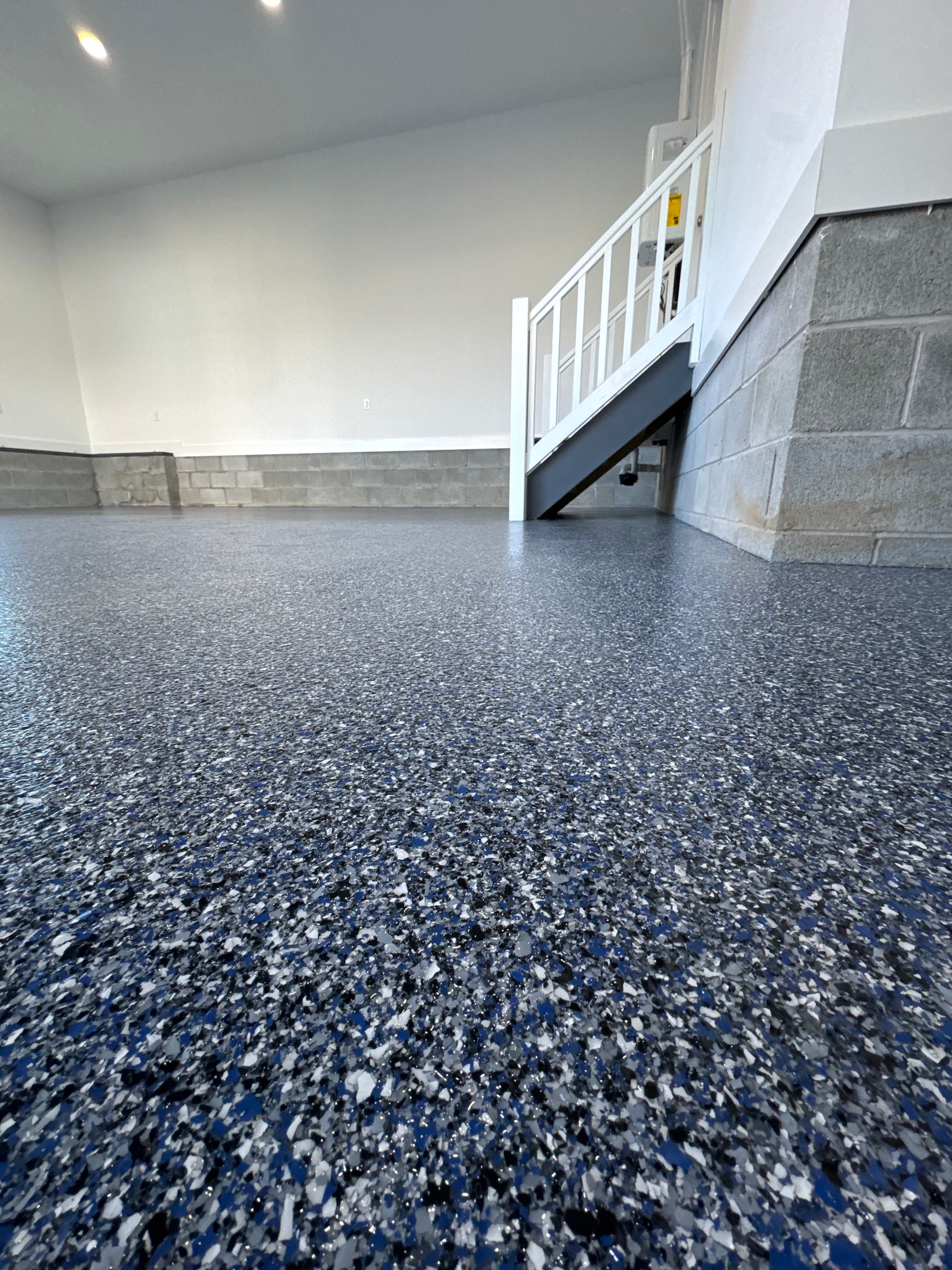 Empty indoor stairwell with speckled floor and white railing against gray walls