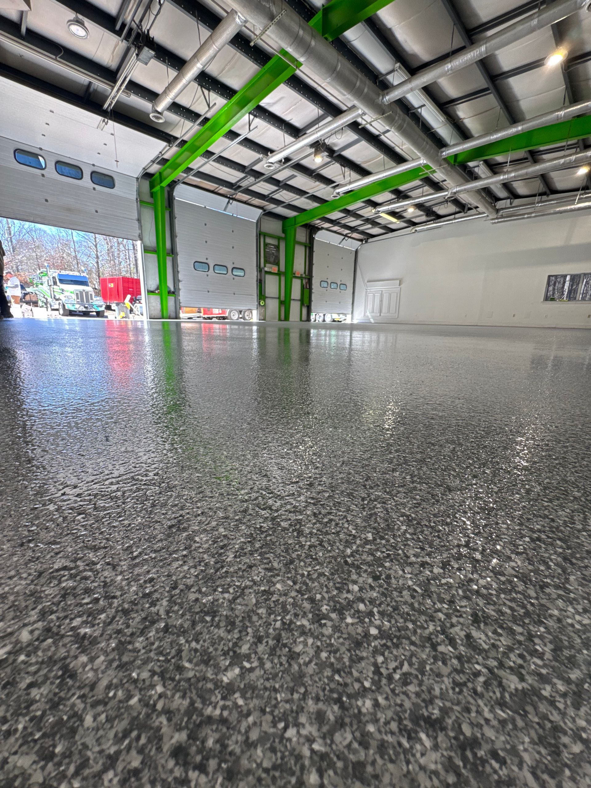 Empty indoor garage with glossy speckled floor, white walls, and green ceiling beams.