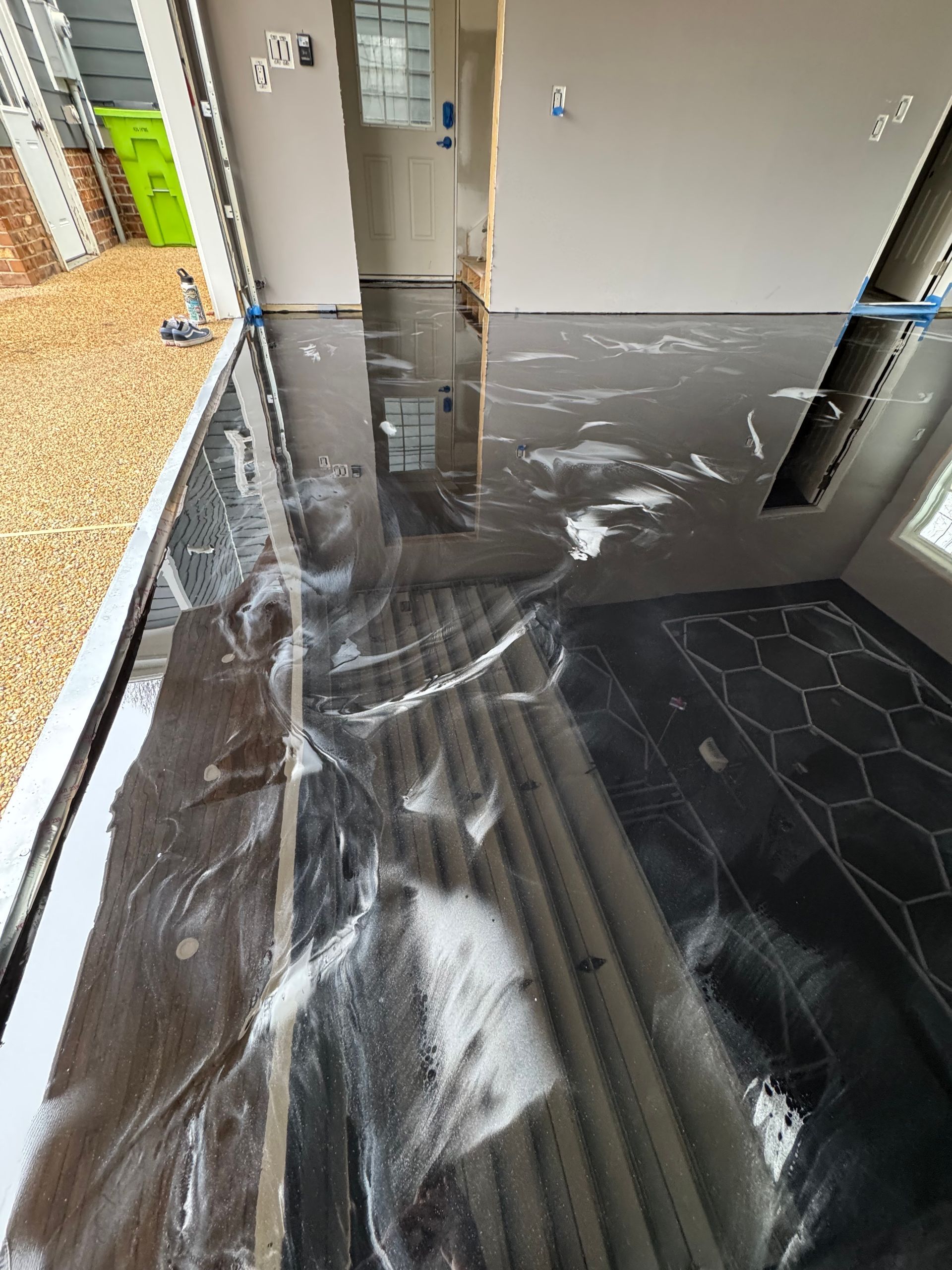 Flooded kitchen floor with standing water reflecting cabinets and a black hex-tile area rug.