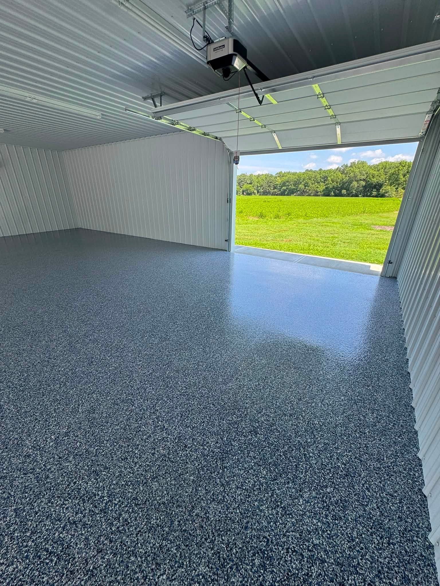 Empty metal storage room with speckled floor and open doorway to a grassy field.