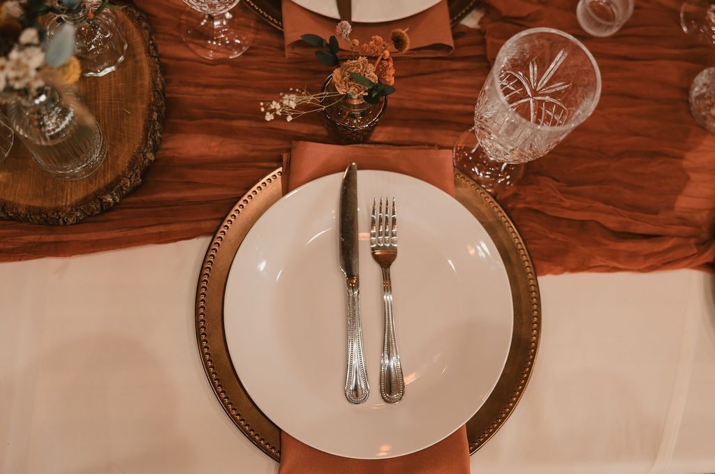 Set dining table with white plate, silverware, glassware, and warm brown decor