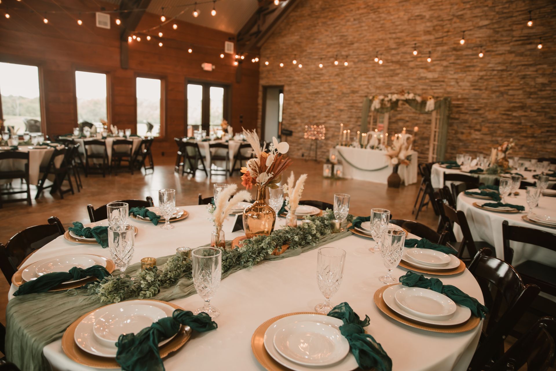 Elegantly set banquet hall with round tables, white tablecloths, green napkins, and stone walls.