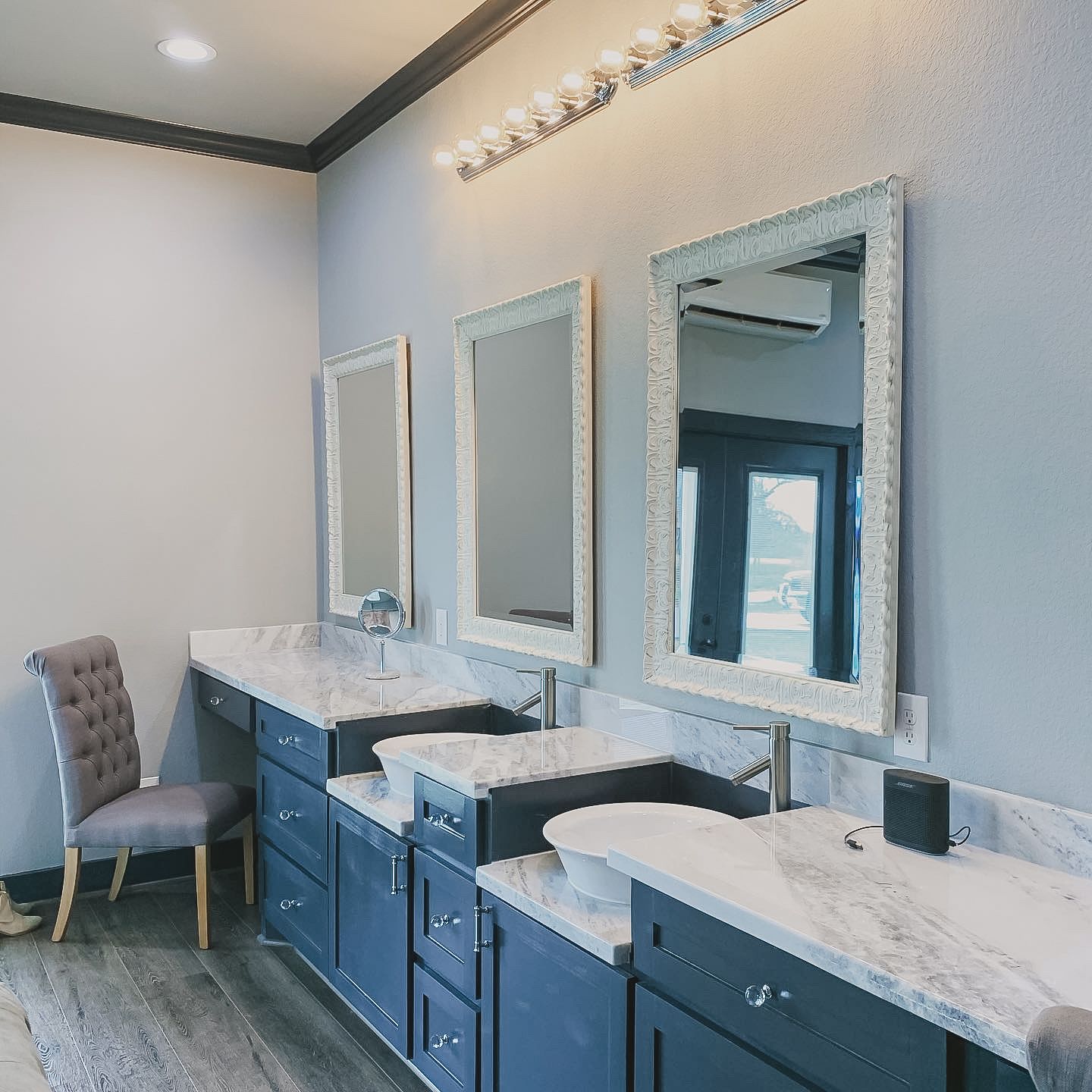 Modern bathroom vanity with blue cabinets, marble countertops, and three framed mirrors under bright lights