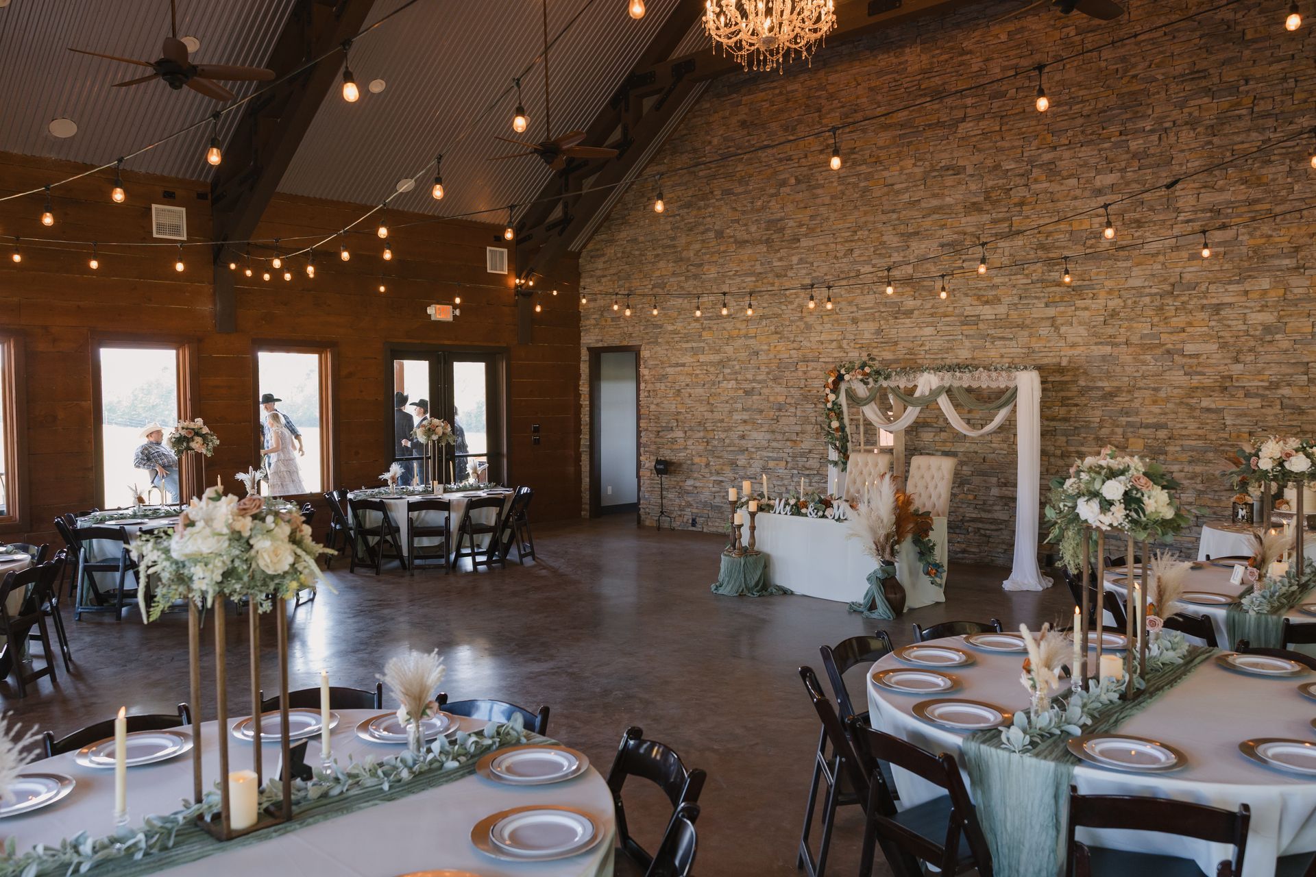 Elegant indoor wedding reception with rustic brick walls, string lights, and floral table settings
