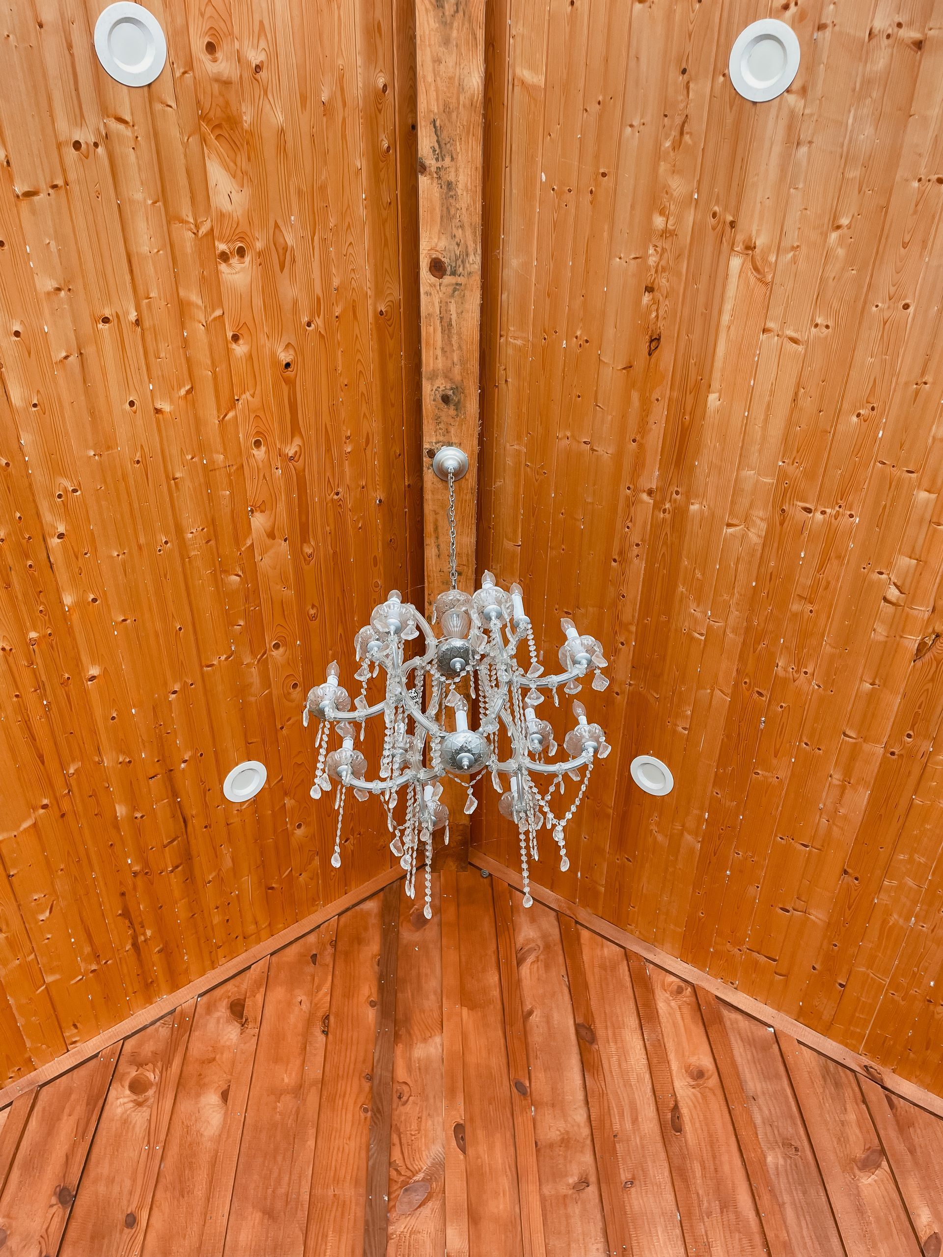 Crystal chandelier hanging in a wooden corner with warm orange-brown walls and floor.