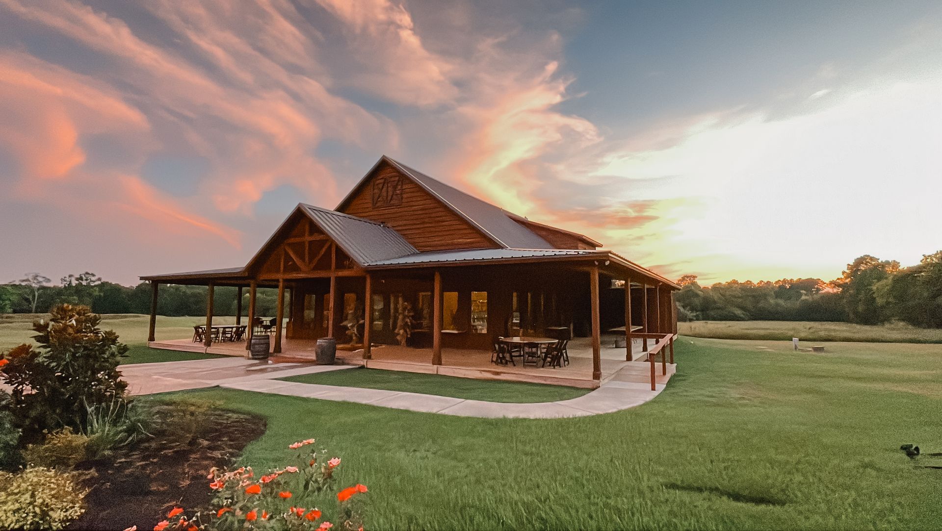 Rustic wooden pavilion with a pointed roof on a green lawn at sunset