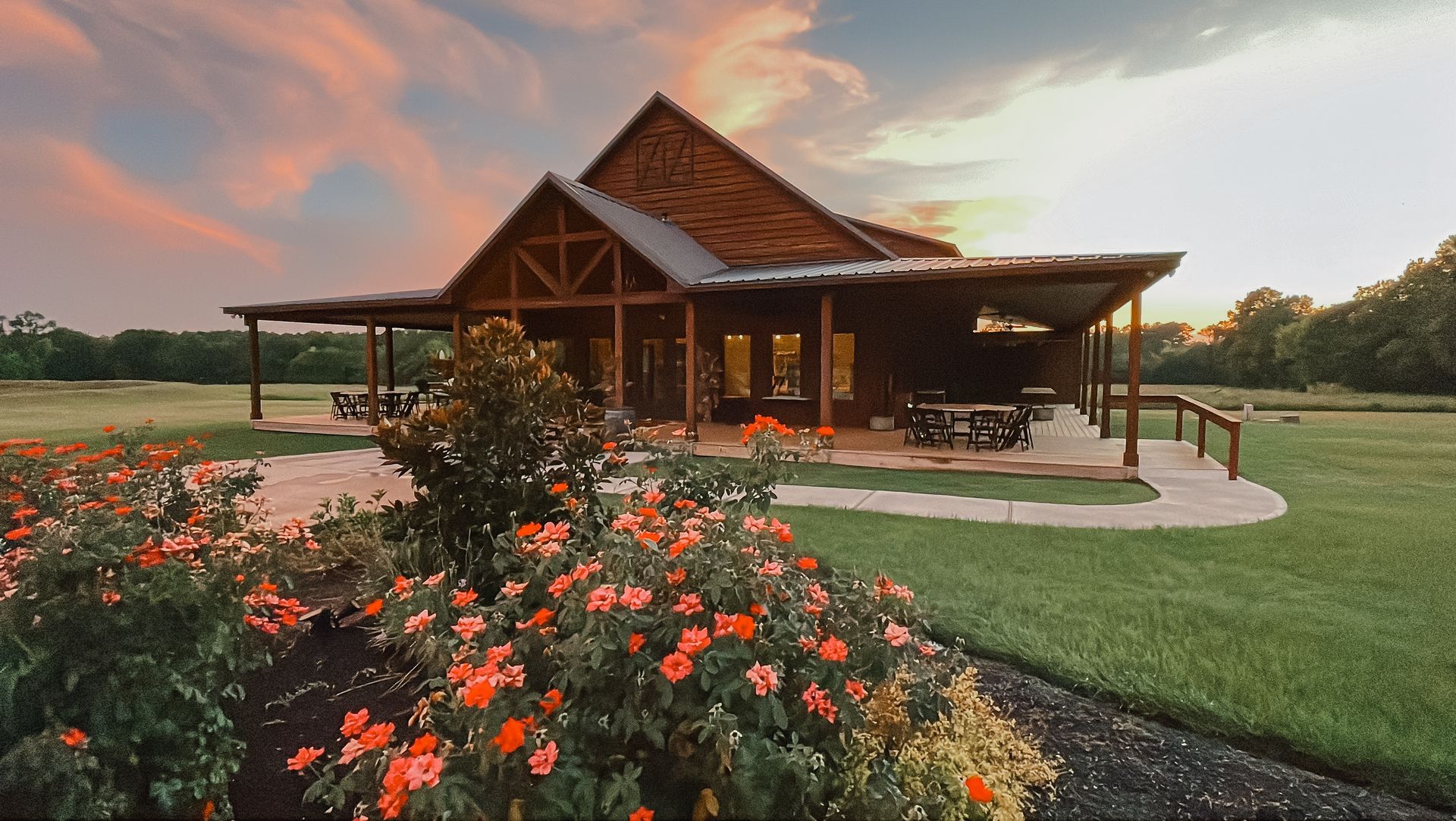 Rustic wooden lodge at sunset with red flowers in the foreground and a grassy lawn