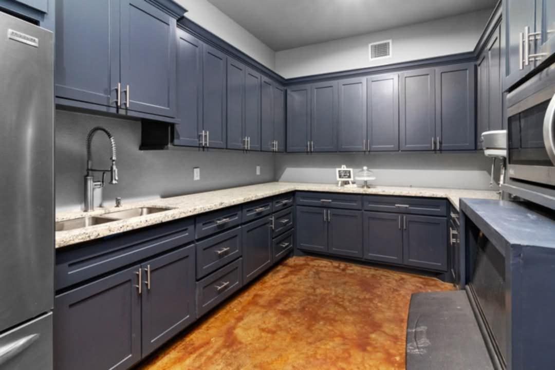 Modern kitchen with dark blue cabinets, stainless appliances, and copper-colored floor.