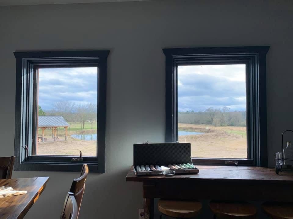 Interior room with two windows overlooking a cloudy landscape and picnic table outside
